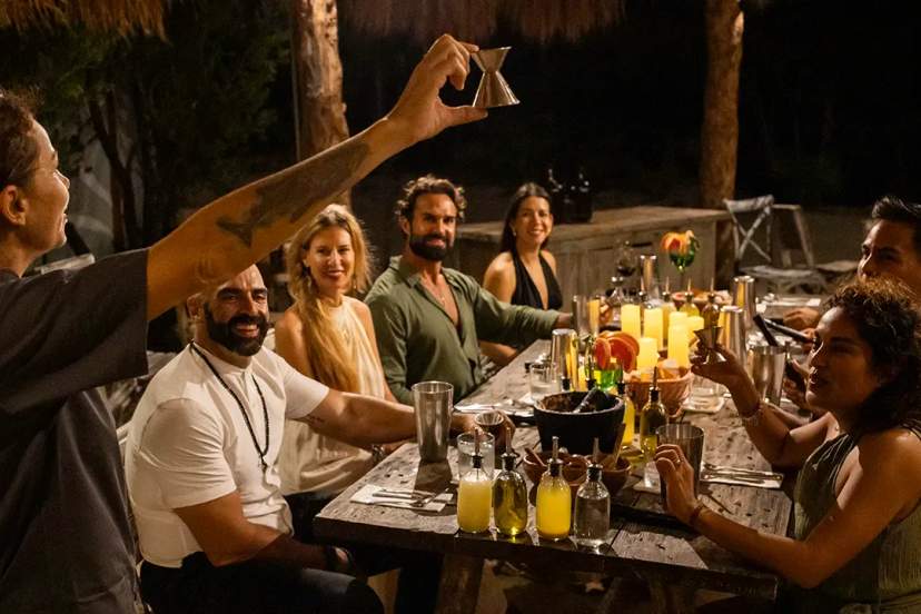 Un animado grupo disfruta cocteles y risas en una cena festiva al aire libre en Experiencia Gourmet en la Riviera Maya