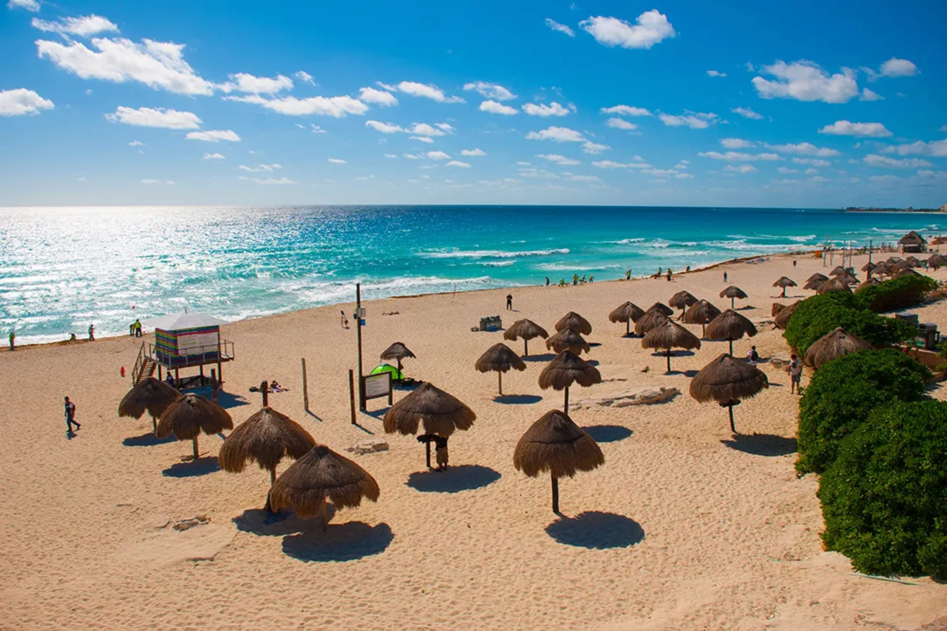 Playa soleada de Cancun con mar Caribe turquesa, arena blanca, palapas y olas suaves bajo cielo azul en Mexico