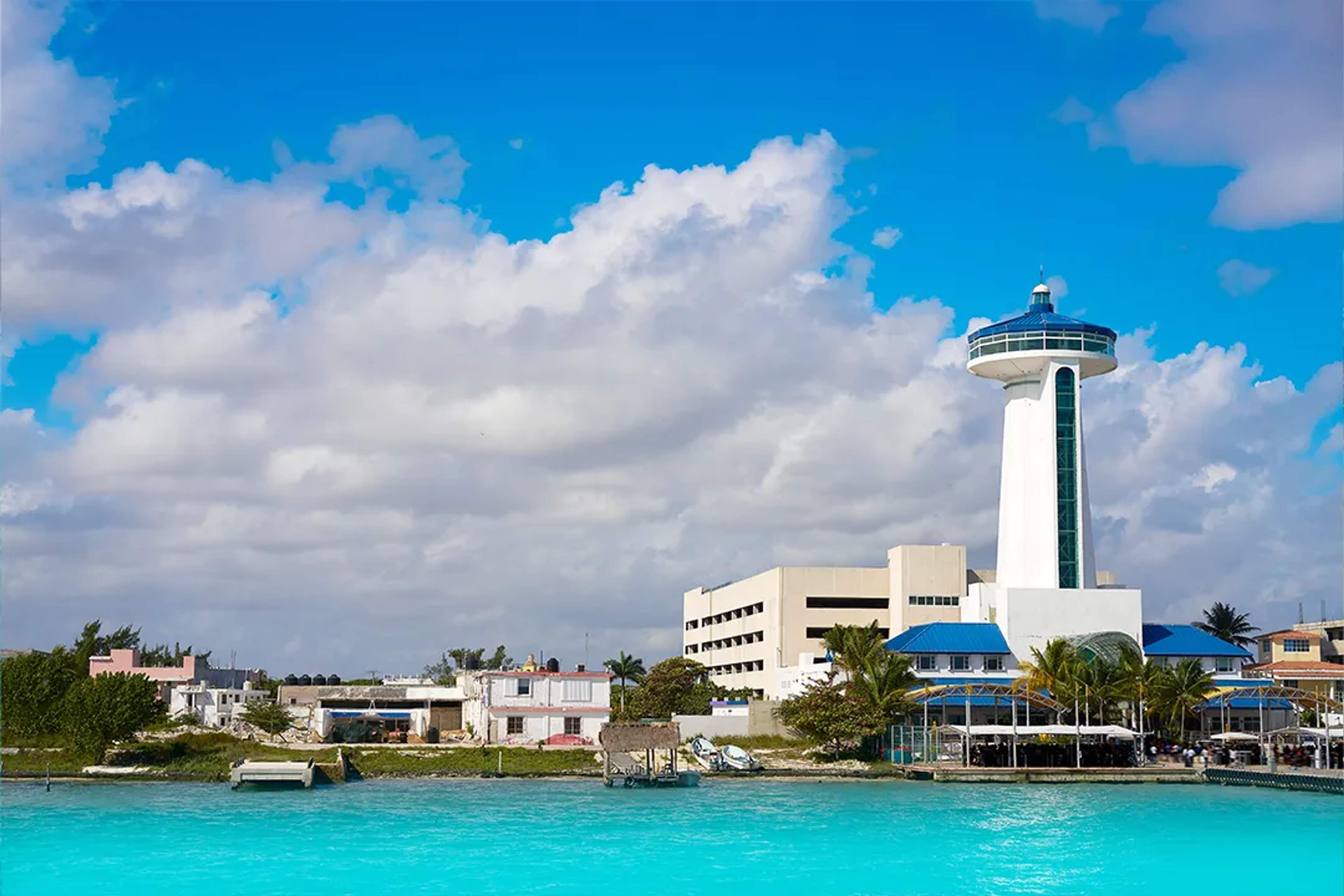 Vista de la torre panorámica y edificios frente al mar en Puerto Juárez, Cancún, bajo cielo azul.