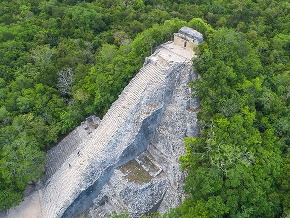 Aerial view of the ancient pyramid in the Coba ruins, surrounded by lush green forest.