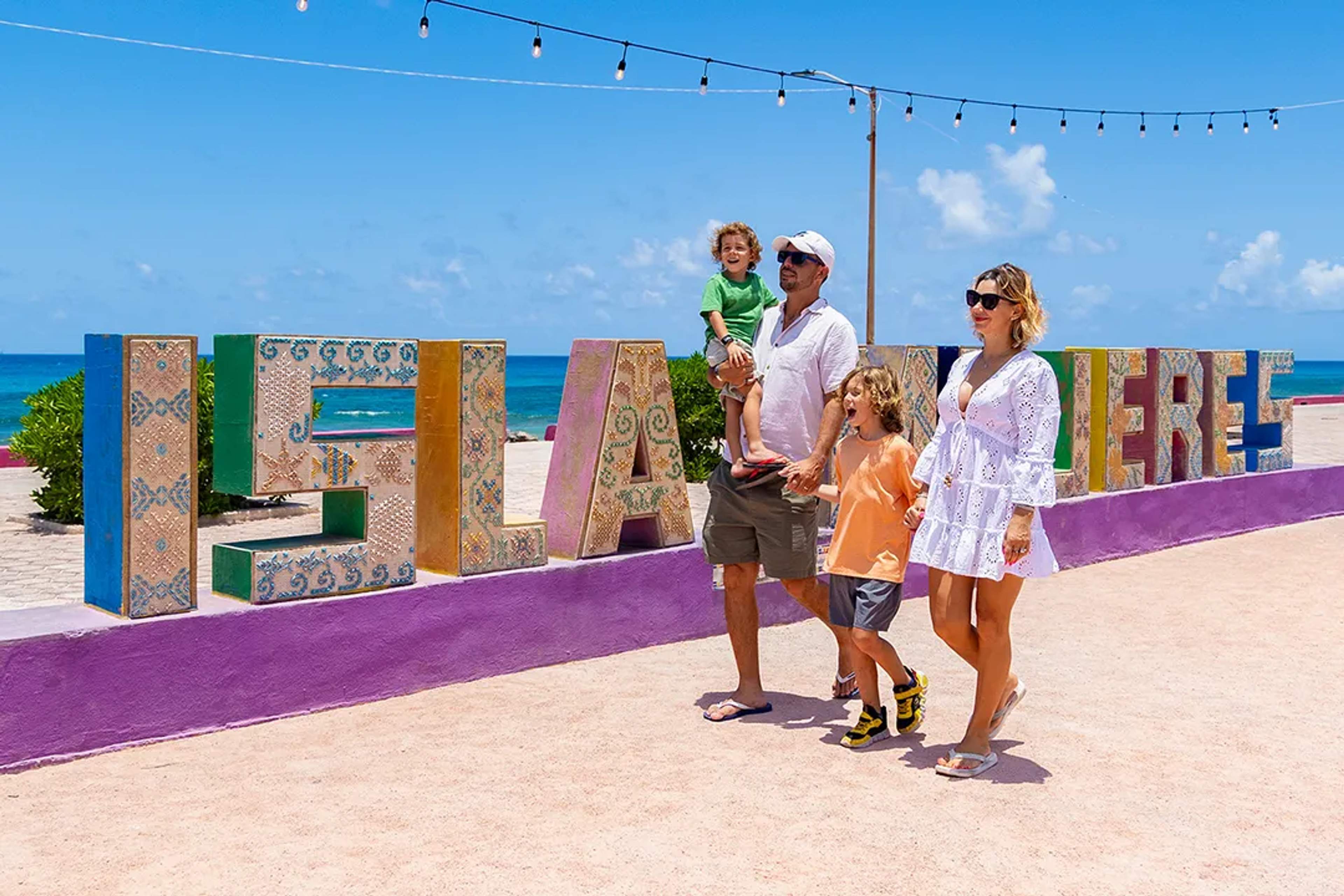 Family walking by Isla Mujeres sign during Cancun family tour with Caribbean ocean views and sunshine