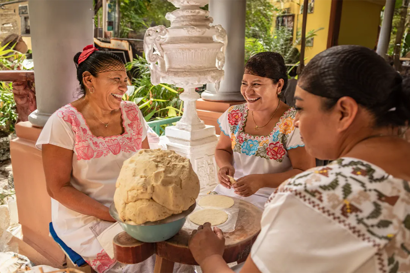 Women in traditional dress preparing tortillas, showcasing Cancun's rich culinary traditions.