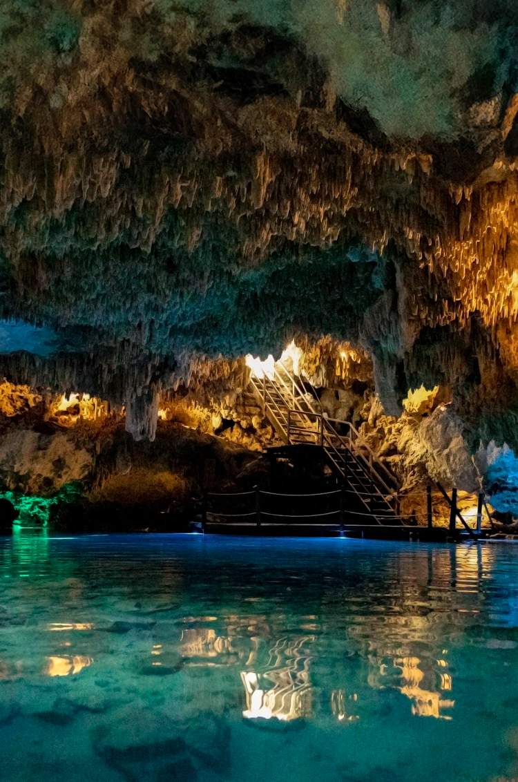 Un cenote fascinante con agua cristalina, iluminado por luces de colores y estalactitas colgando del techo de la cueva.