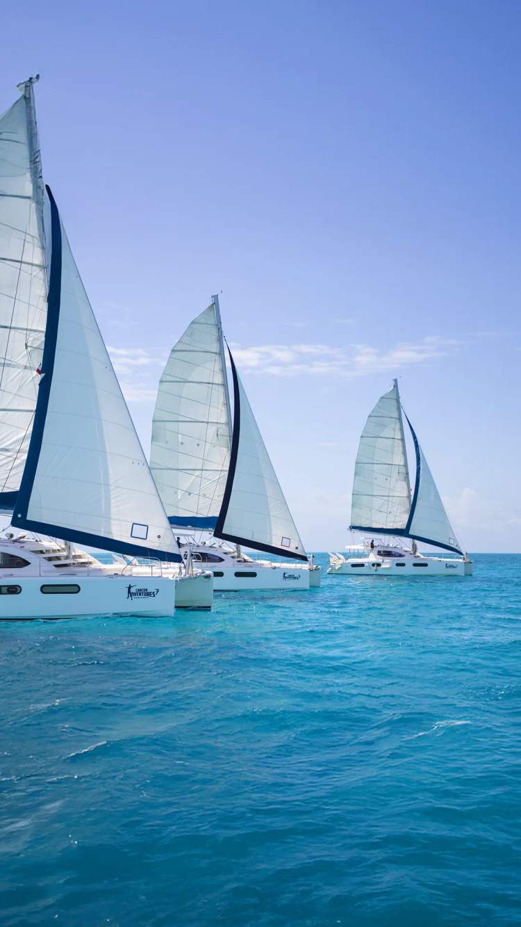 Three sailing catamarans lined up, part of a Cancun corporate event.