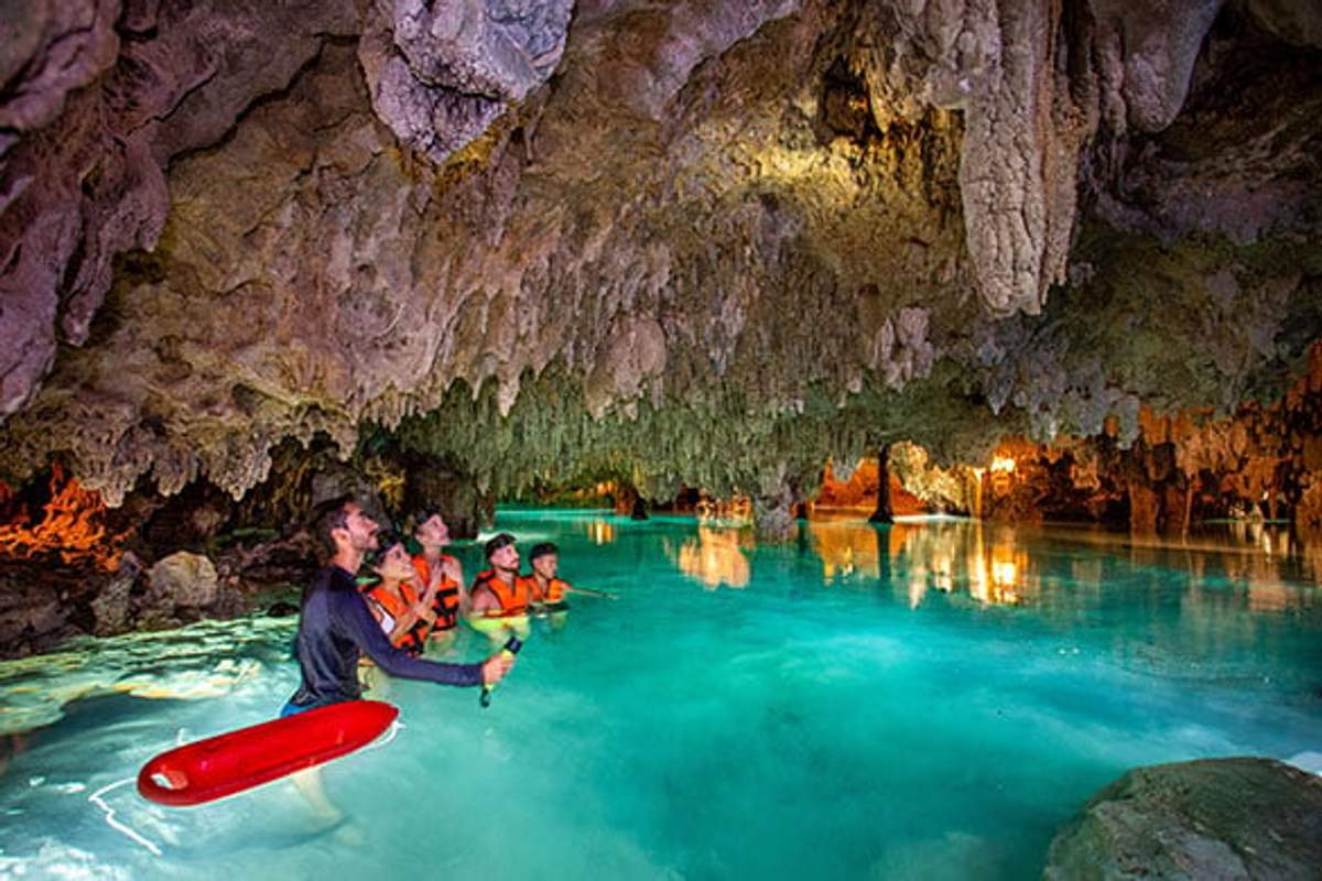 Personas exploran una cueva subterránea con agua cristalina y estalactitas iluminadas.