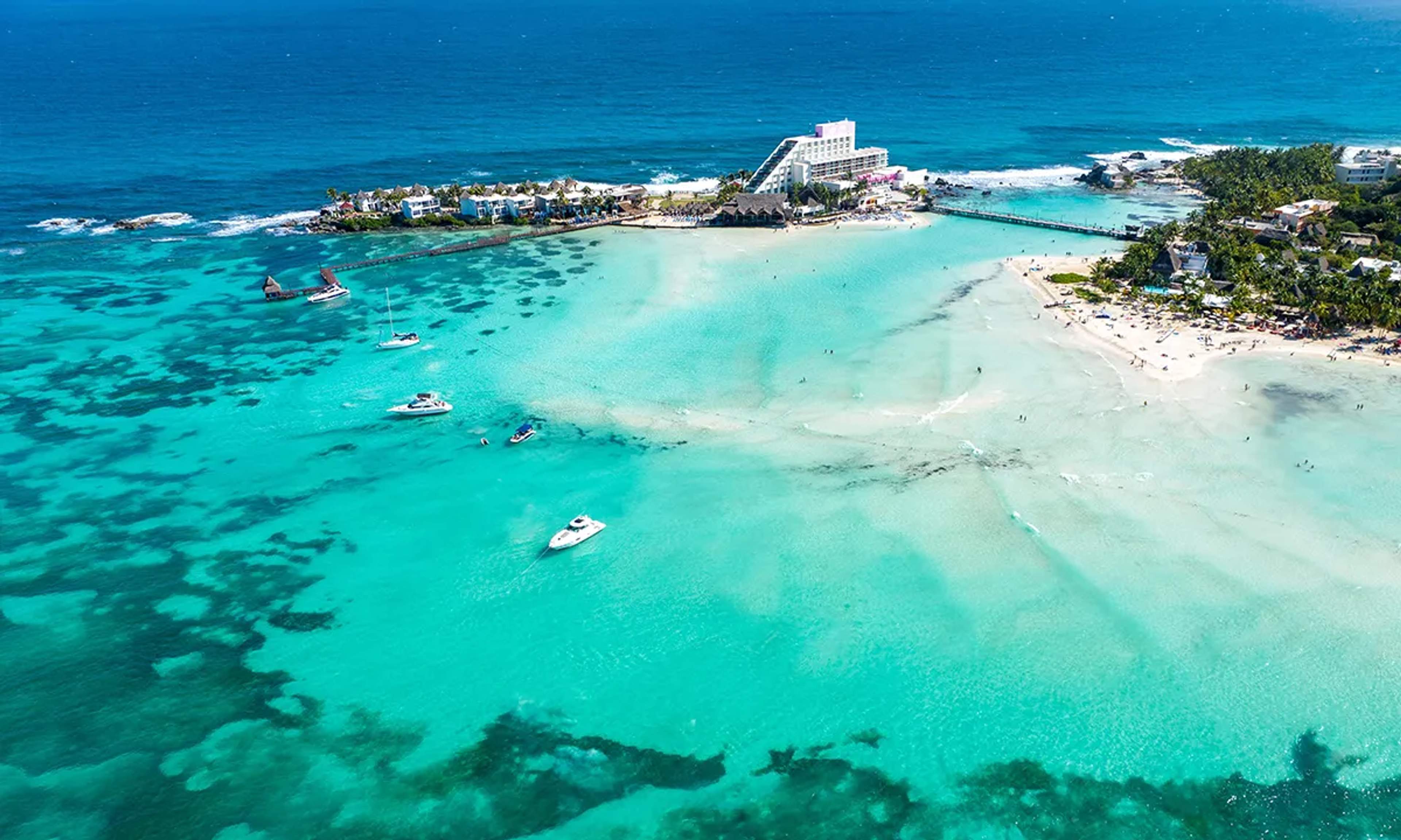 Aerial view of a Caribbean beach with turquoise waters and boats floating in a tropical paradise.