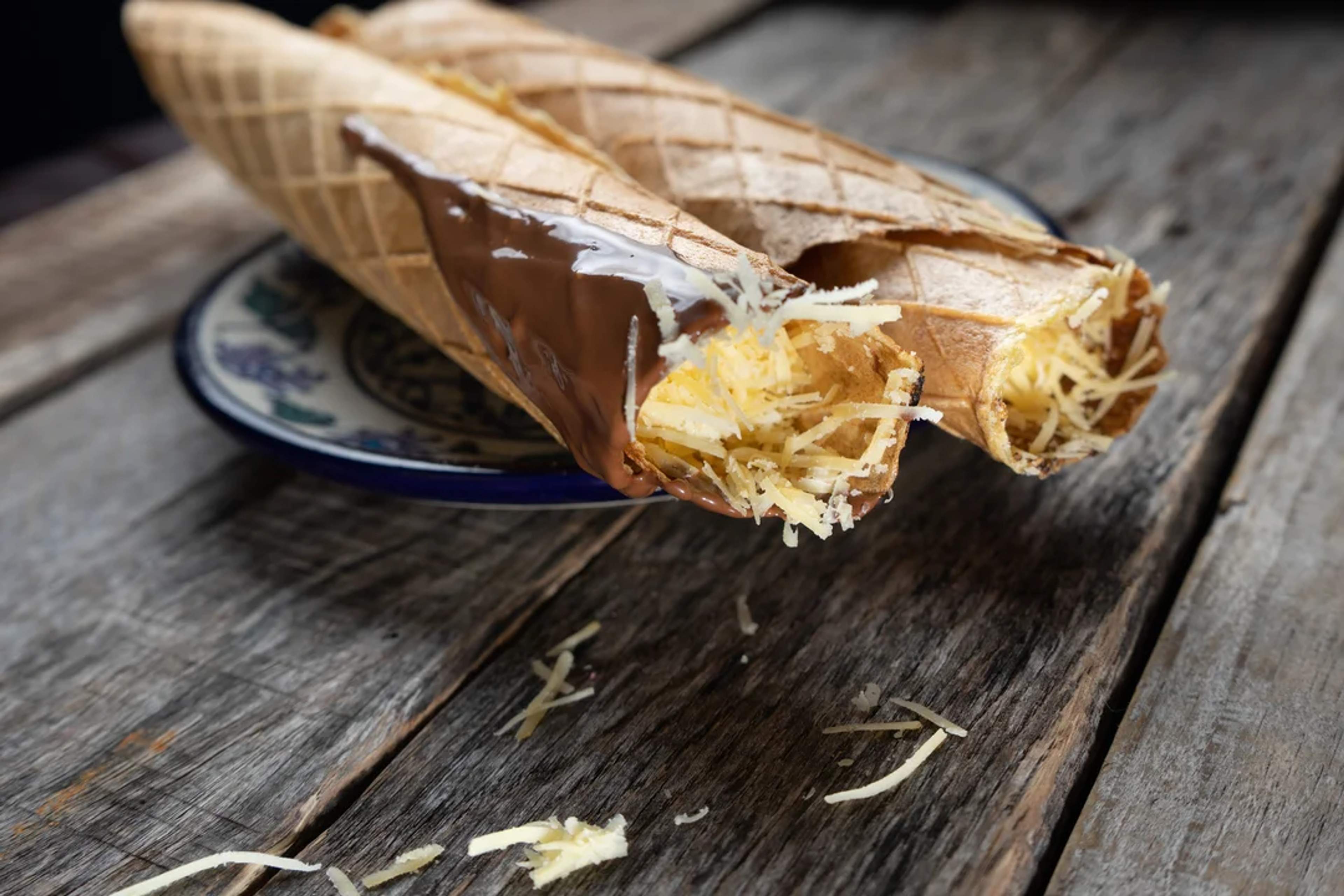 Sweet wafers filled with shredded cheese and dipped in chocolate, served on a rustic plate.