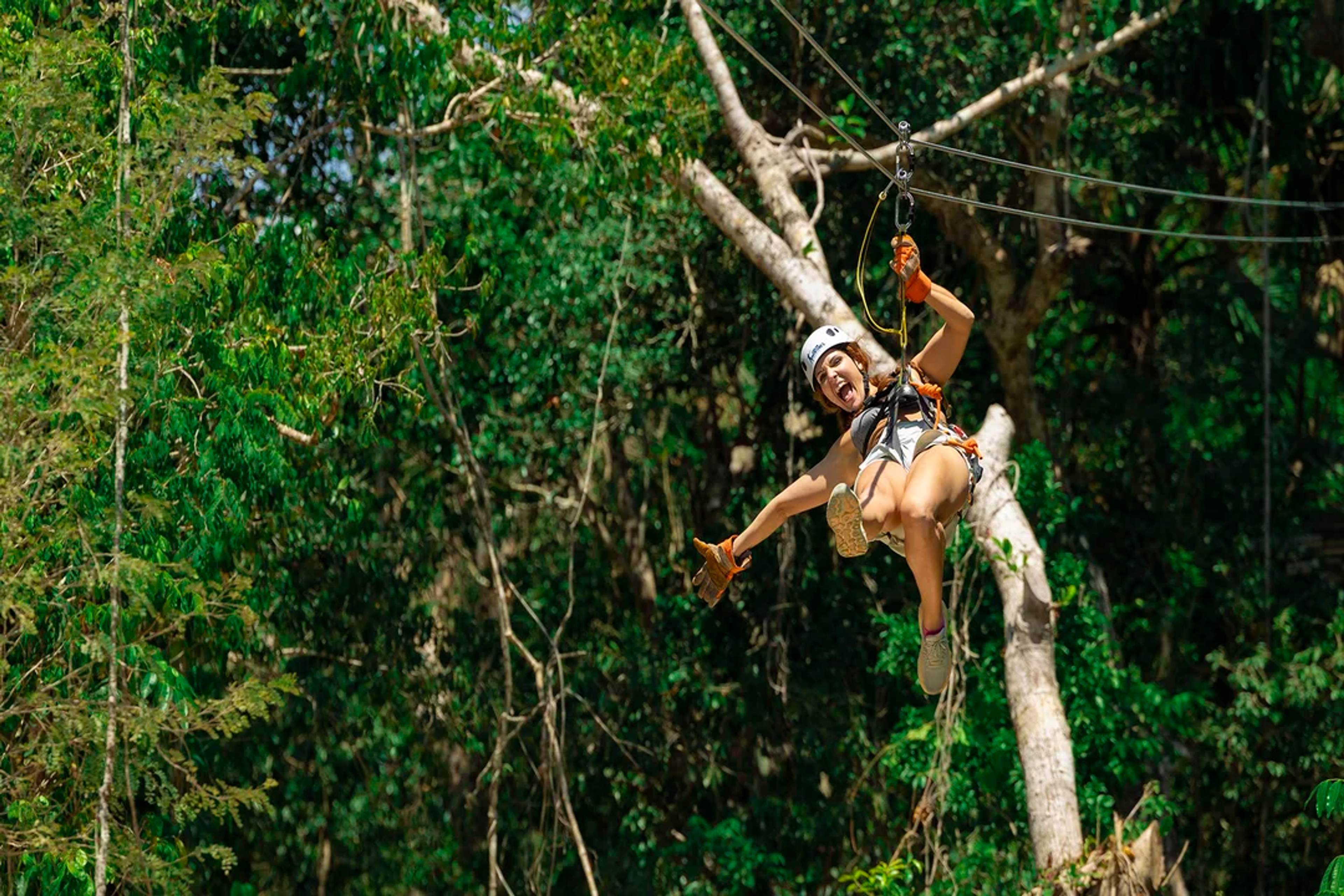 Una mujer disfruta de una emocionante tirolesa en la selva, sintiendo la adrenalina de la aventura.