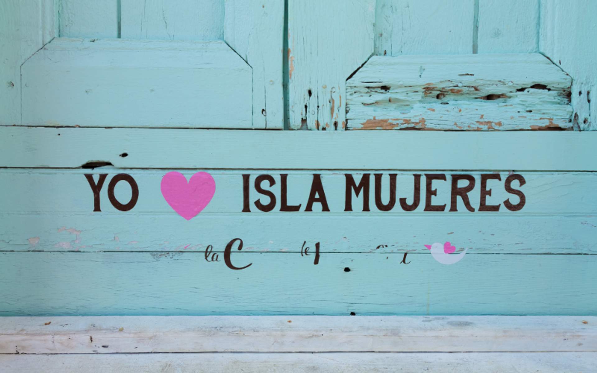 A turquoise wall with the text "Yo ♥ Isla Mujeres" painted on it, showing love for the island.