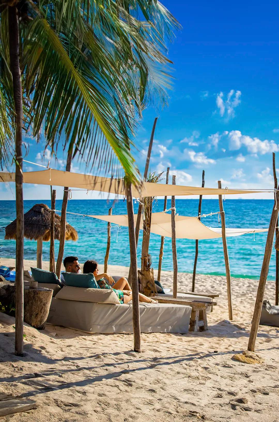 A couple lounging on a beach under shaded canopies at Punta Venado Beach Club in Cancun.