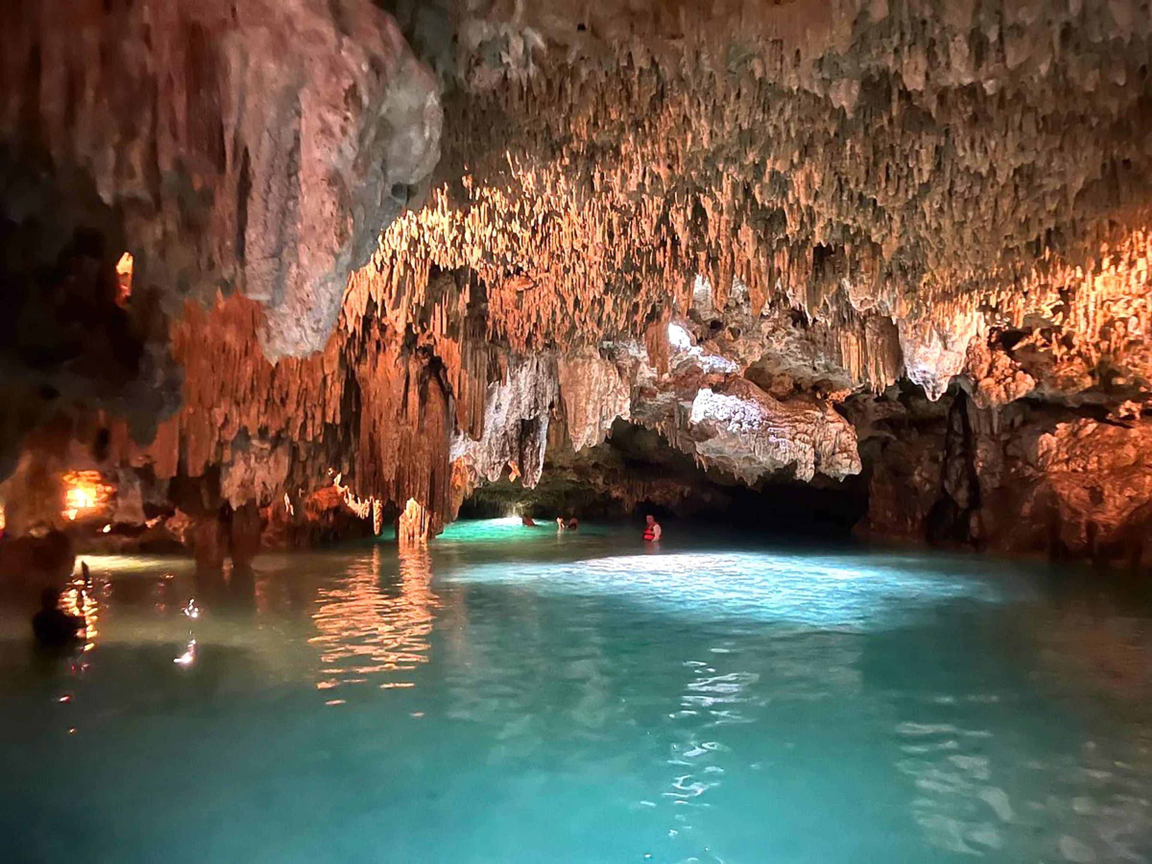 Nadadores explorando las aguas cristalinas dentro de un impresionante cenote adornado con estalactitas en Cancún.