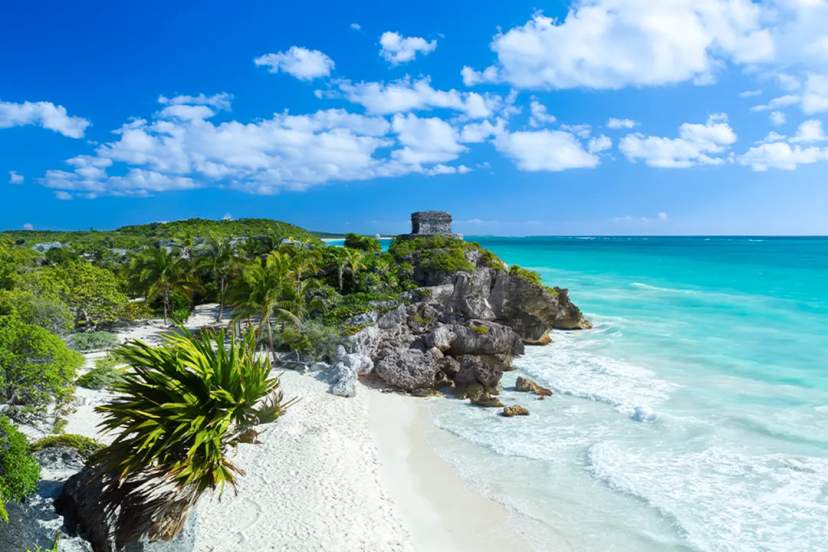 Stunning beach at Tulum with turquoise water, white sand, and ancient Mayan ruins on a cliff.