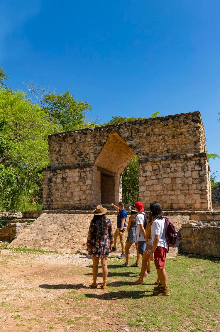 Group of tourists exploring an ancient Mayan arch in Ek Balam, surrounded by lush vegetation.