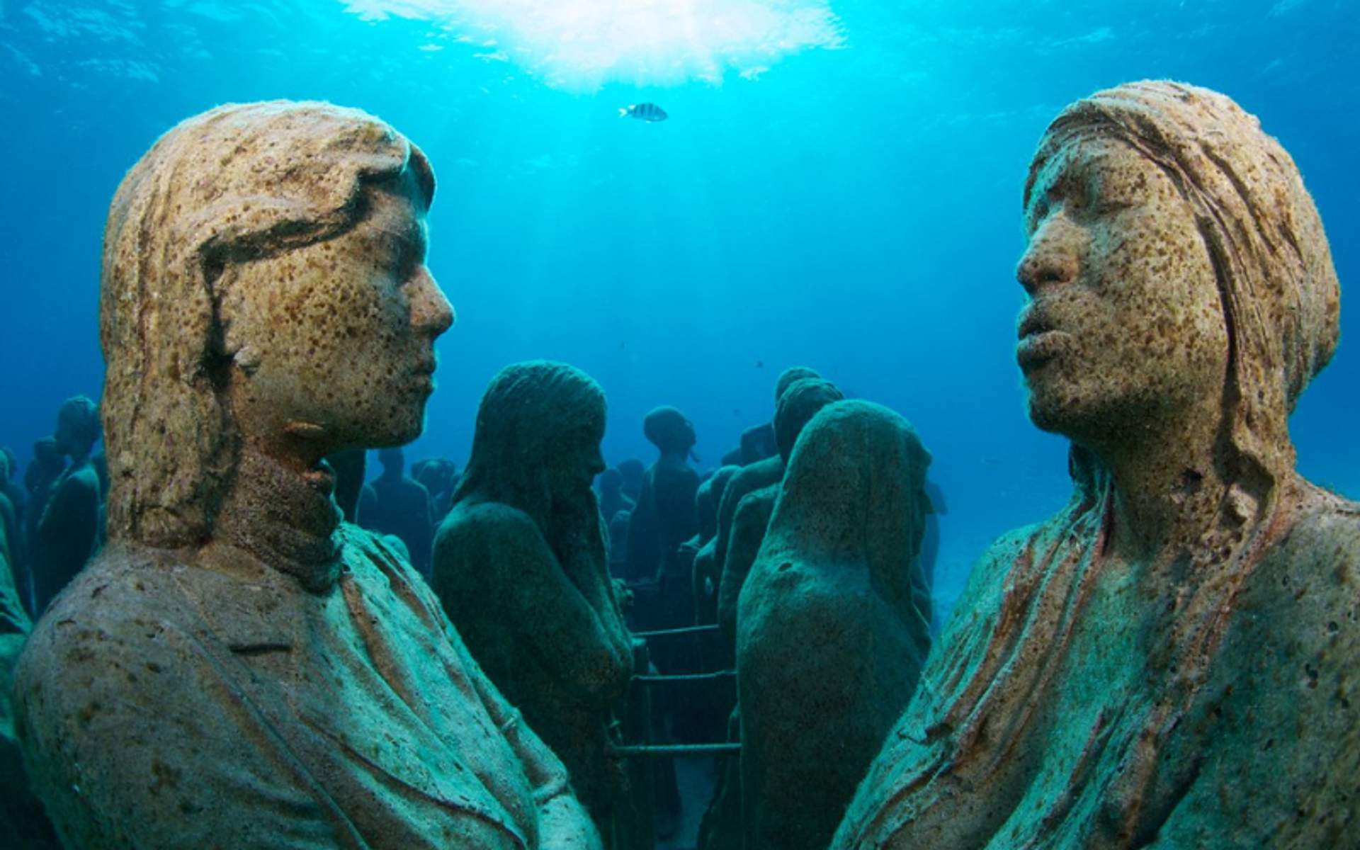 Underwater statues at the Cancun Underwater Museum (MUSA), creating an eerie yet beautiful scene in the clear blue ocean.