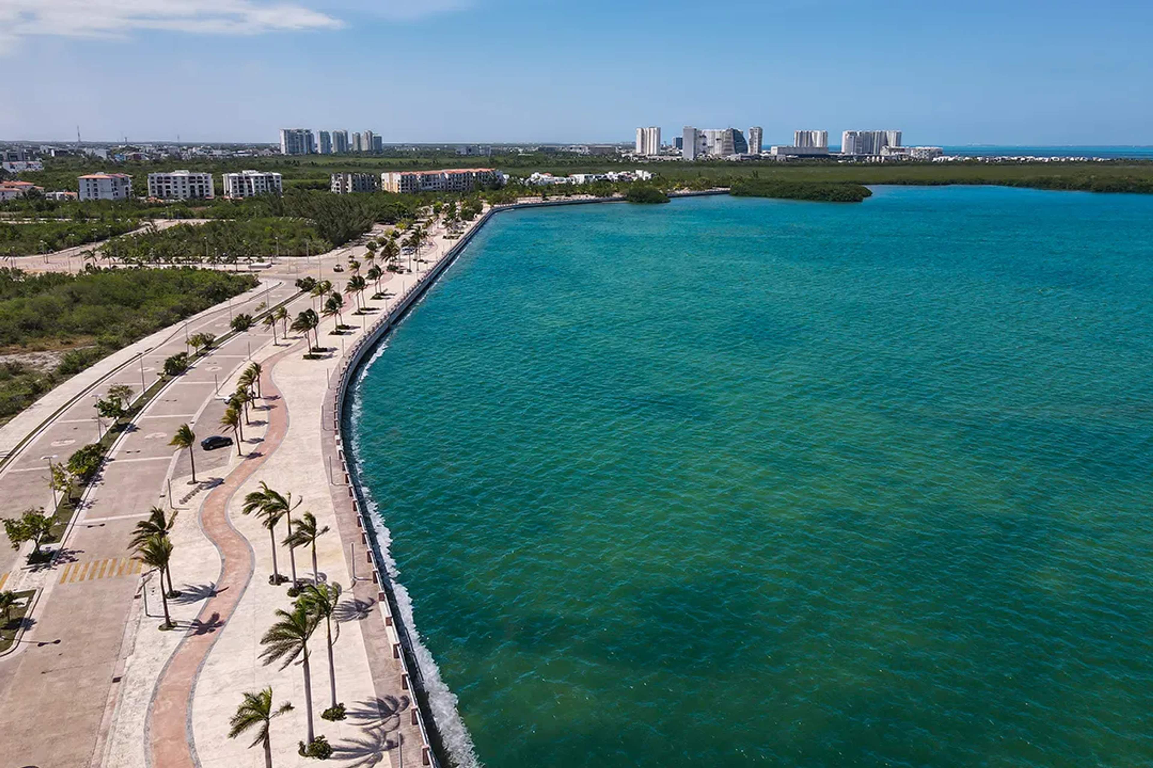 Aerial view of Malecón Tajamar in Cancún, Mexico, with turquoise lagoon, palm trees, and city skyline.