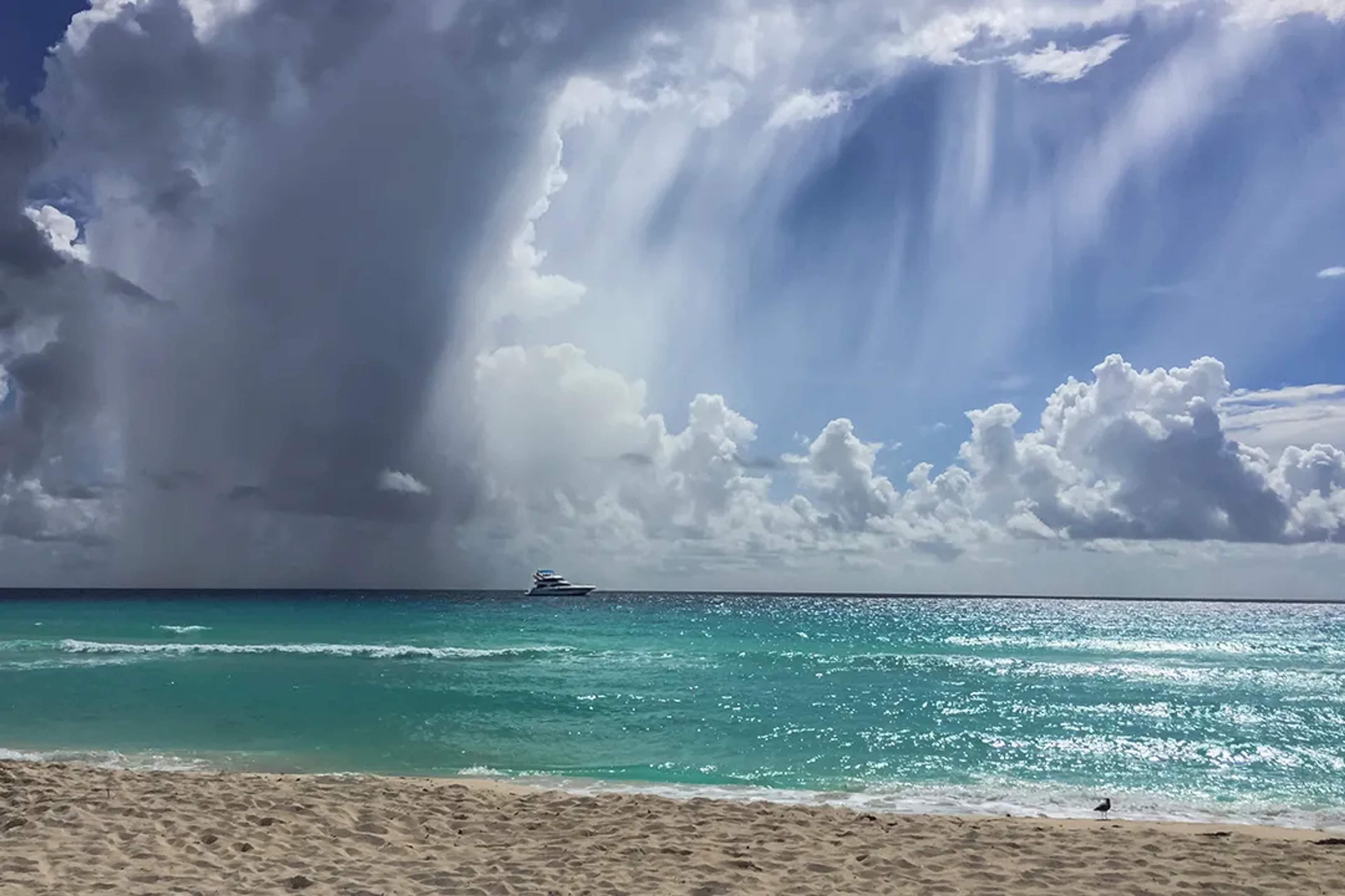 Cancun beach with turquoise Caribbean waters yacht at sea and dramatic rain clouds under tropical sky