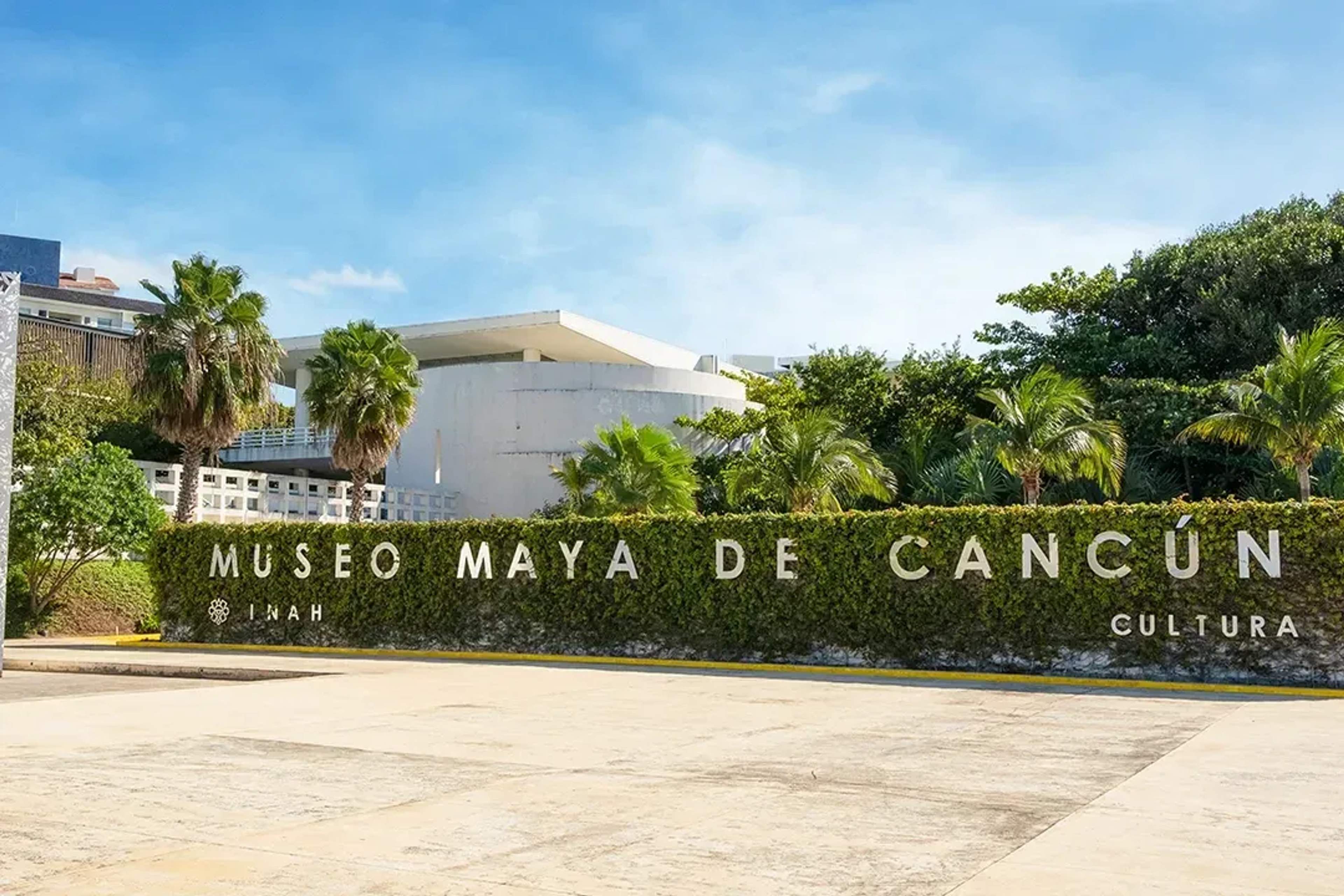 Exterior view of the Museo Maya de Cancún, surrounded by palm trees and modern architecture.