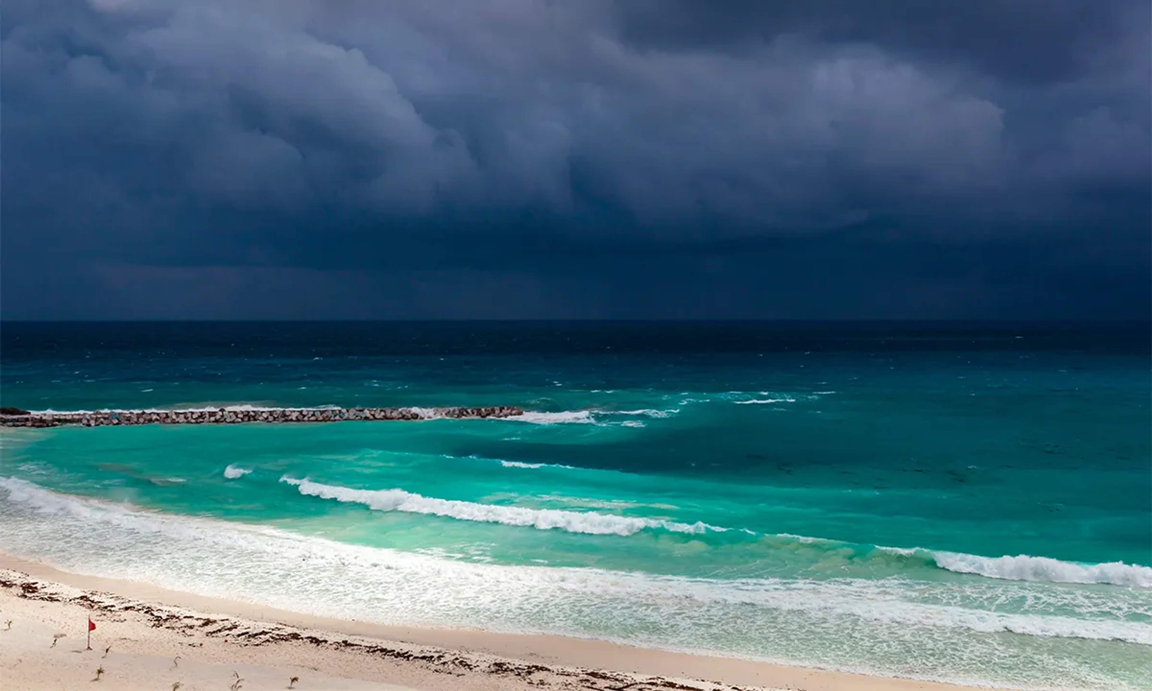 A Cancun beach with turquoise waters under a dark, stormy sky, creating a dramatic scene.