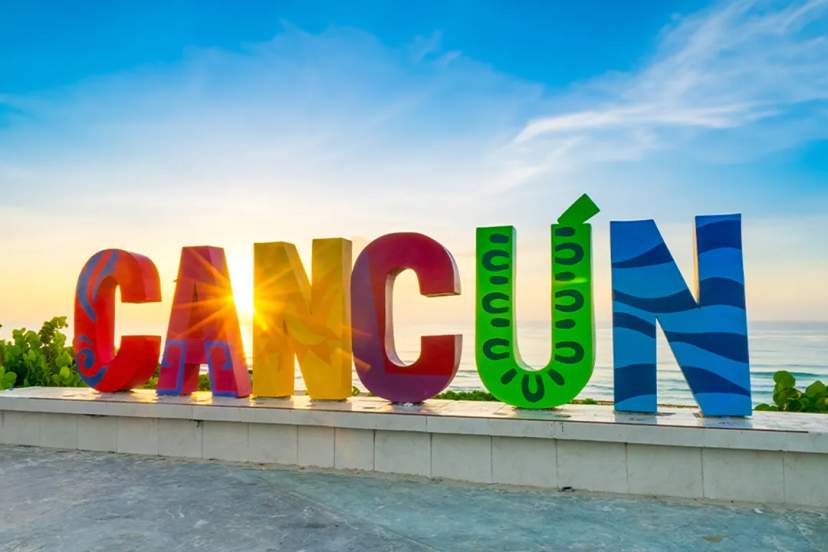 Letrero colorido de "CANCÚN" junto al mar, un lugar popular para fotos de turistas y vacacionistas.