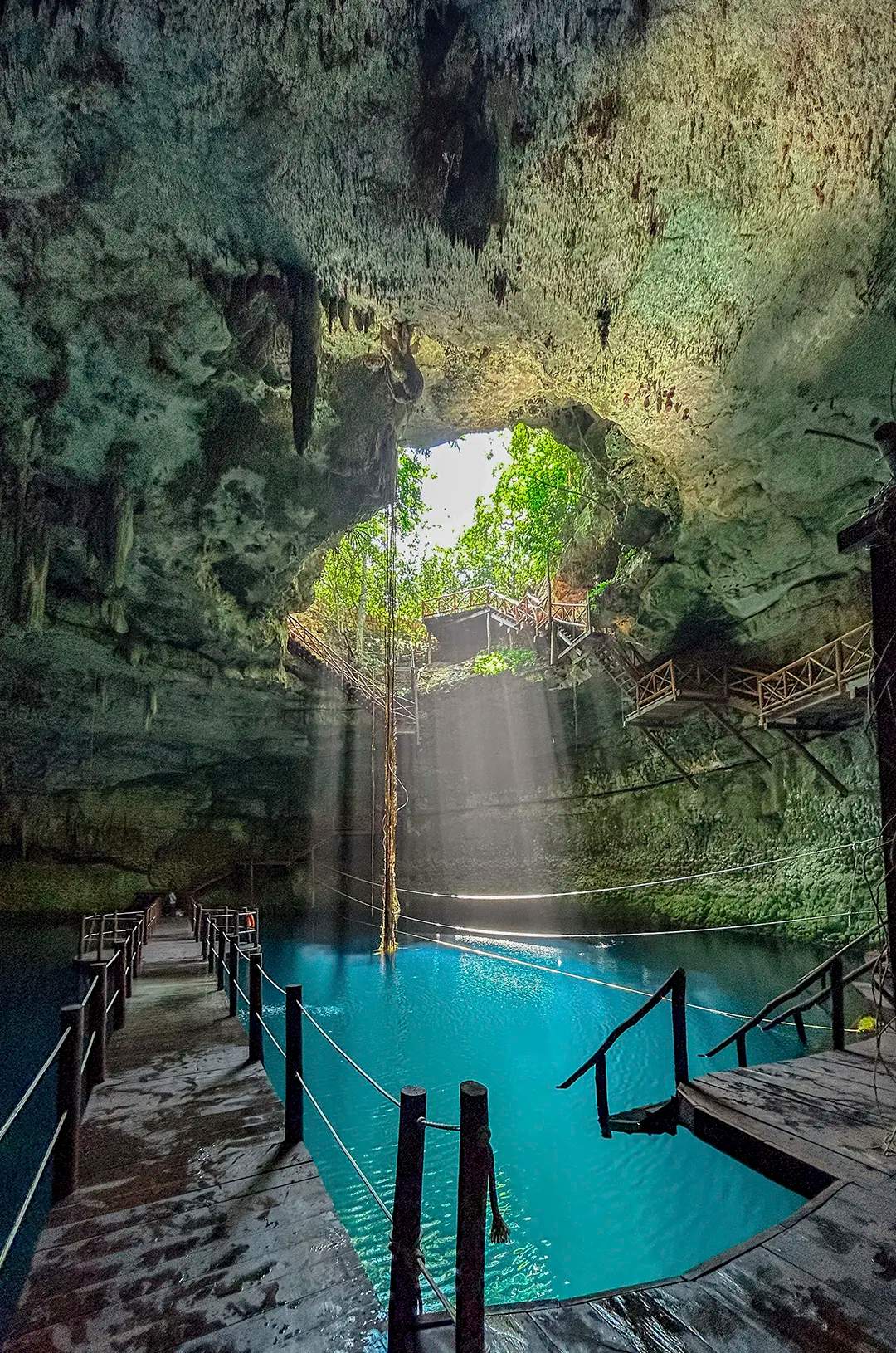 Sunlight streams into a stunning cenote, illuminating its turquoise waters and ancient cave formations in Yalcobá.