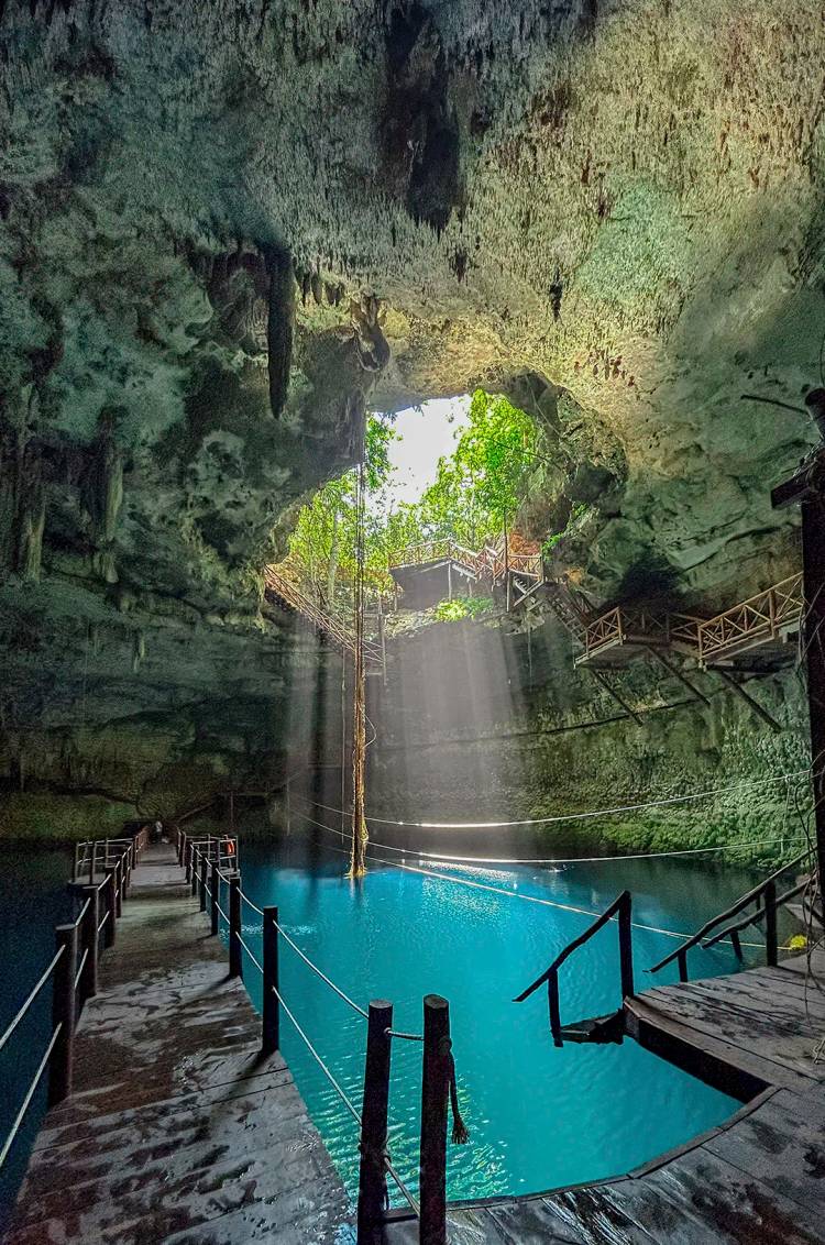 Cenote with crystal-clear water and natural light filtering through the top opening.