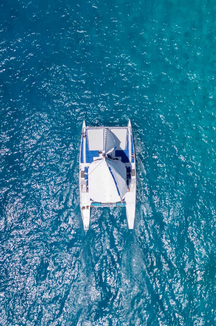 Aerial view of a catamaran sailing on clear turquoise waters.