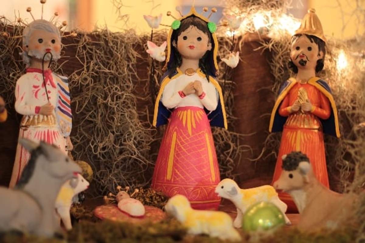 Escena de nacimiento colorida con figuras de María, José y un rey, rodeadas de animales y el niño Jesús, ambientada en un entorno rústico con musgo decorativo y luces cálidas.