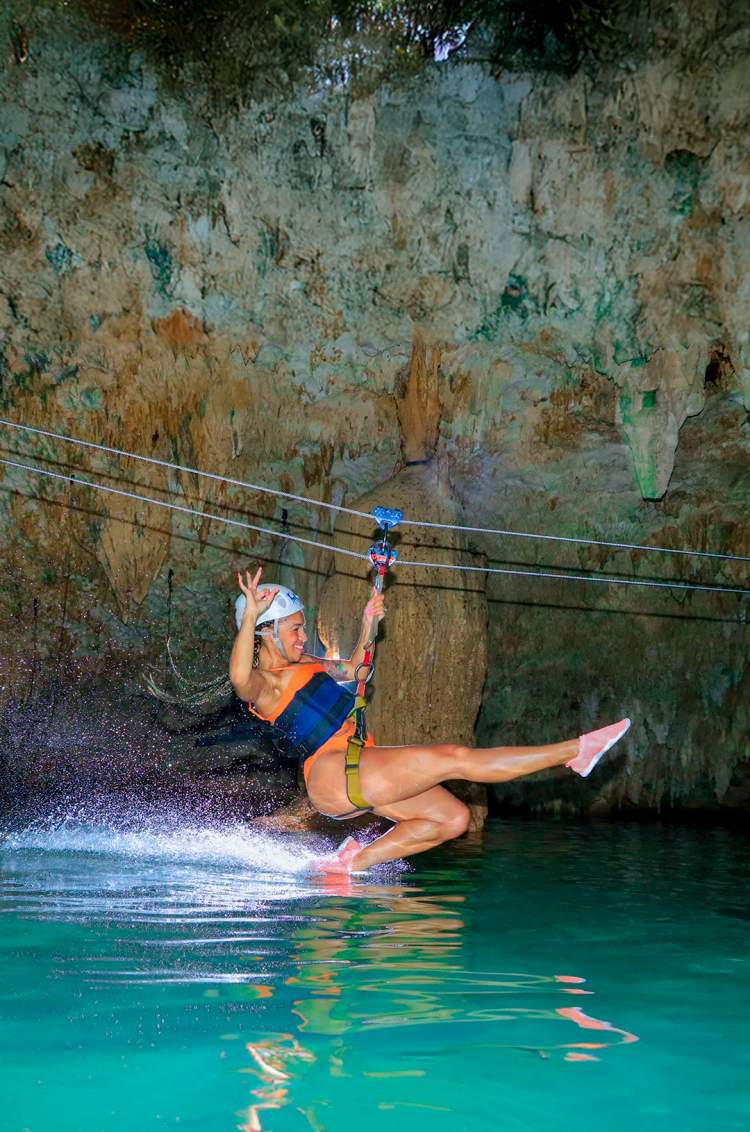 Chica deslizándose en una tirolesa en un cenote subterráneo en Cancún.