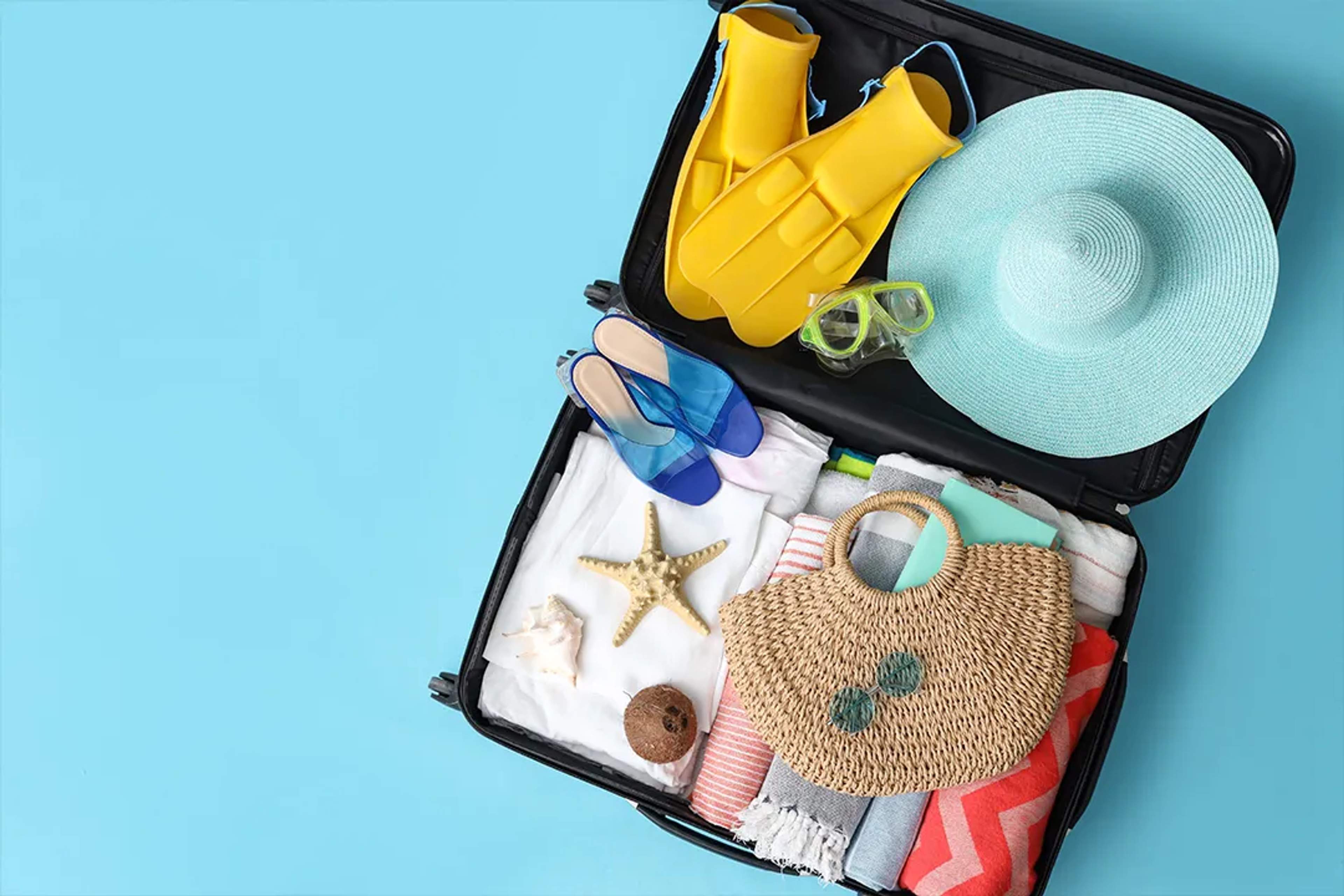 Open suitcase with beachwear, fins, hat, and summer essentials for a Cabo vacation packing guide