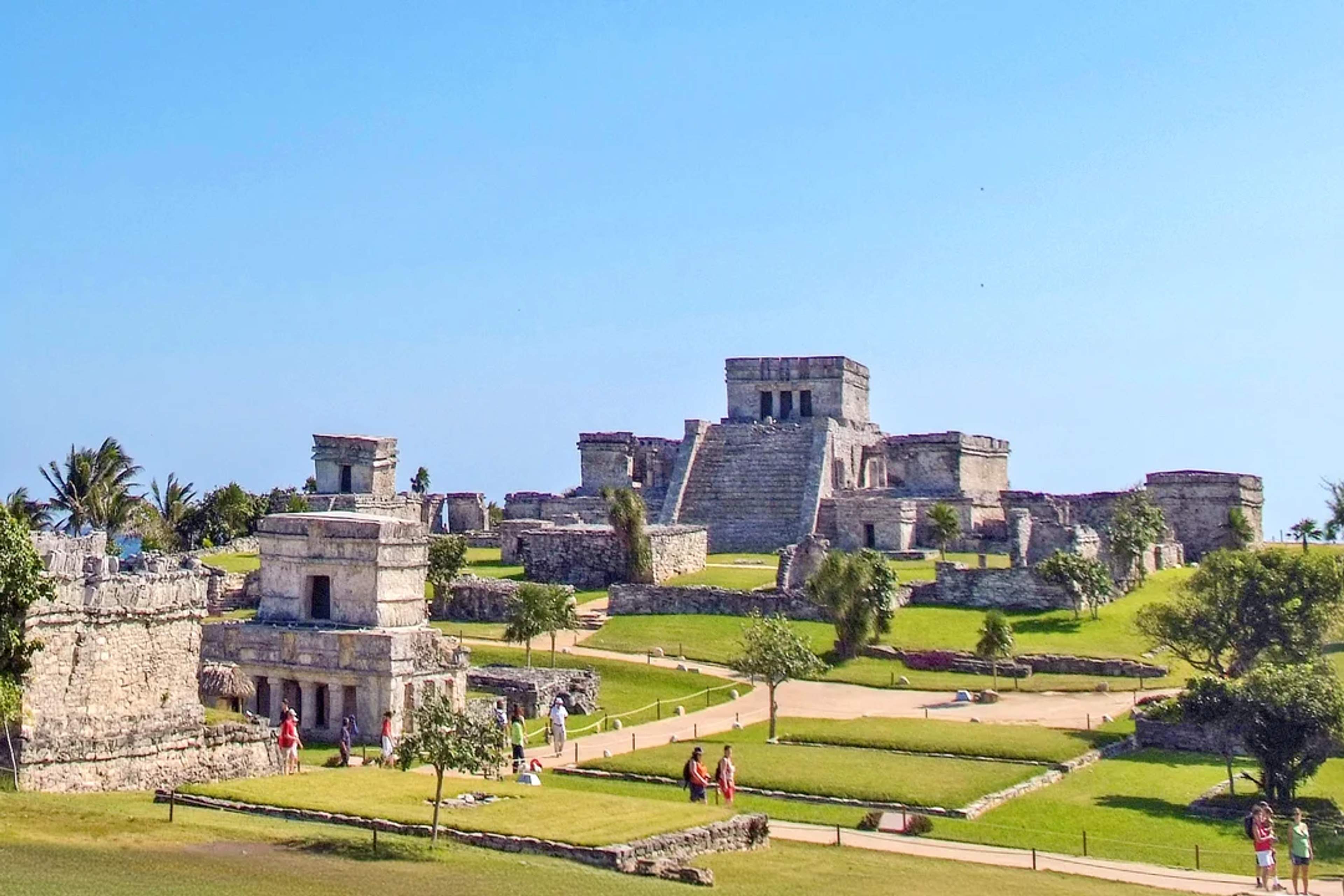 Ancient Tulum ruins overlook the sea, surrounded by lush greenery and clear blue skies.