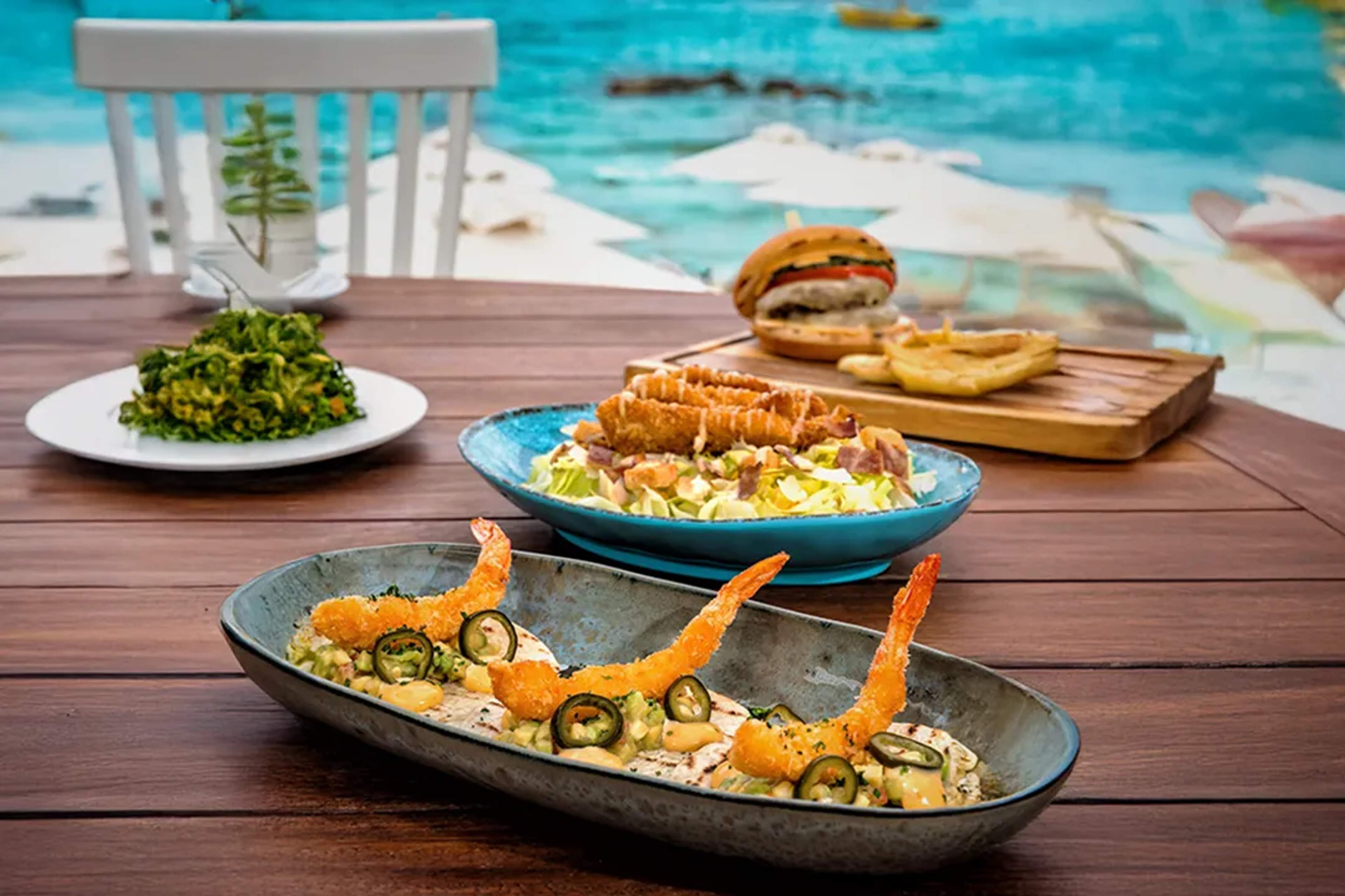 Platos de mariscos y comida frente a la playa sobre mesa de madera con vista al mar turquesa en Cancún