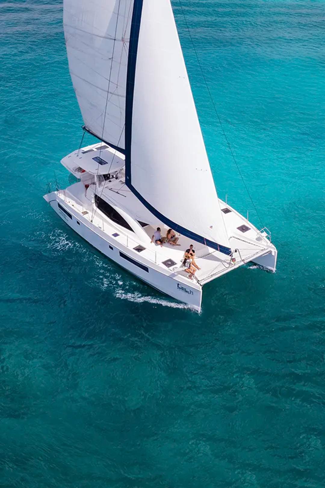 Catamarán blanco navegando en aguas turquesas bajo un cielo azul claro con nubes esponjosas.