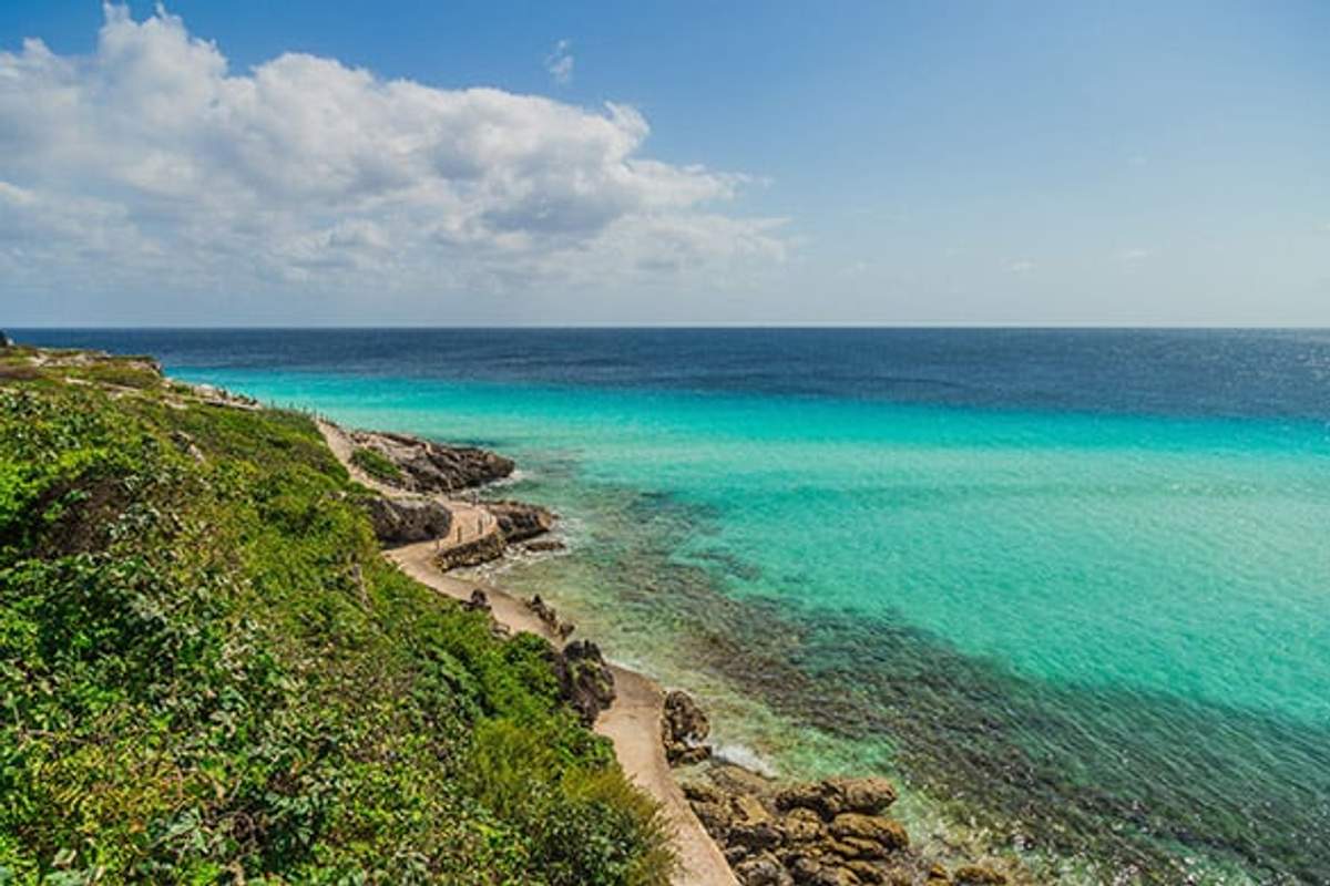 Vista panorámica de las aguas turquesas y la costa rocosa en el Parque Natural Arrecife Garrafón en Isla Mujeres, bajo un cielo parcialmente nublado.