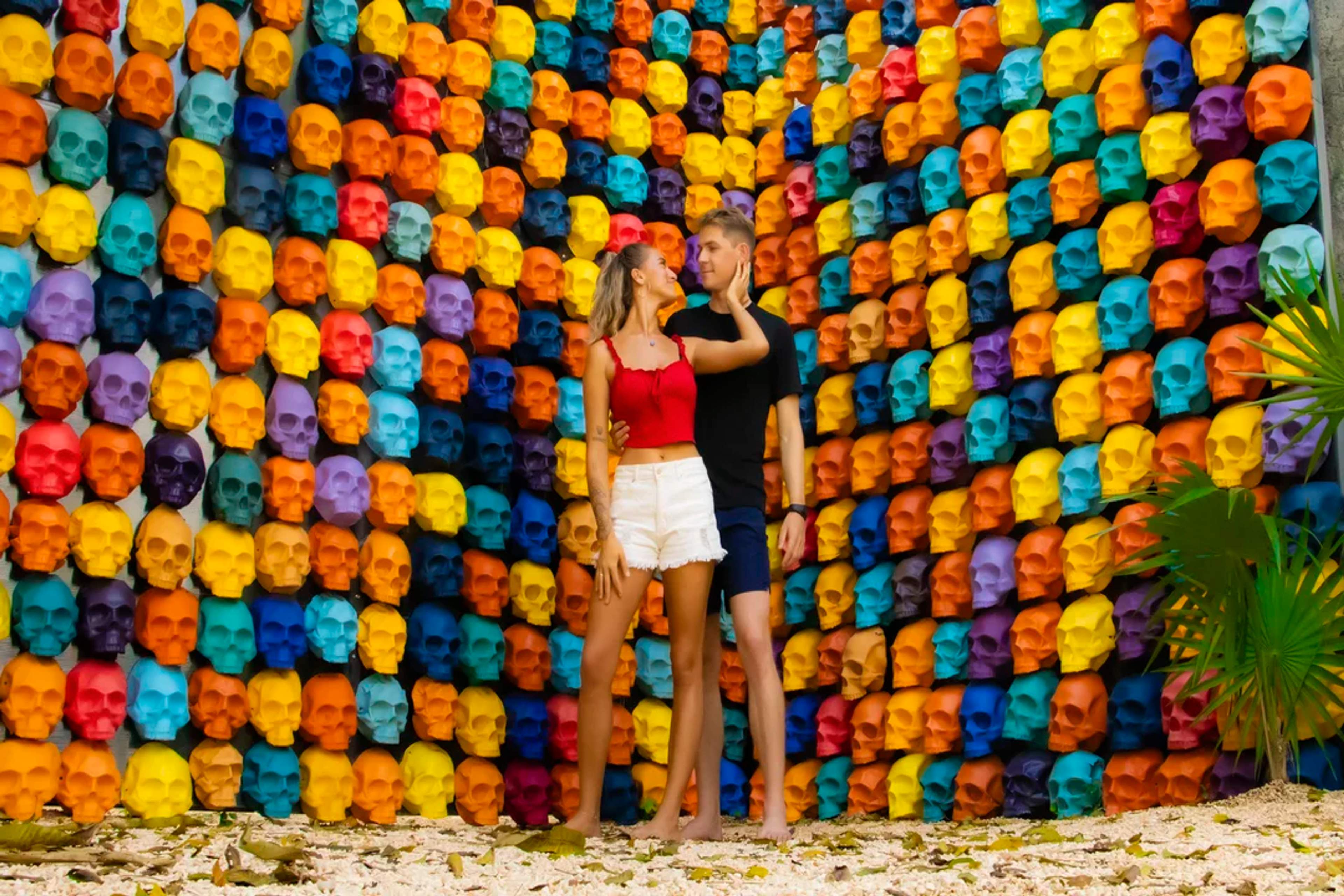 Pareja posando frente a un colorido mural de calaveras en una atracción artística en Tulum.