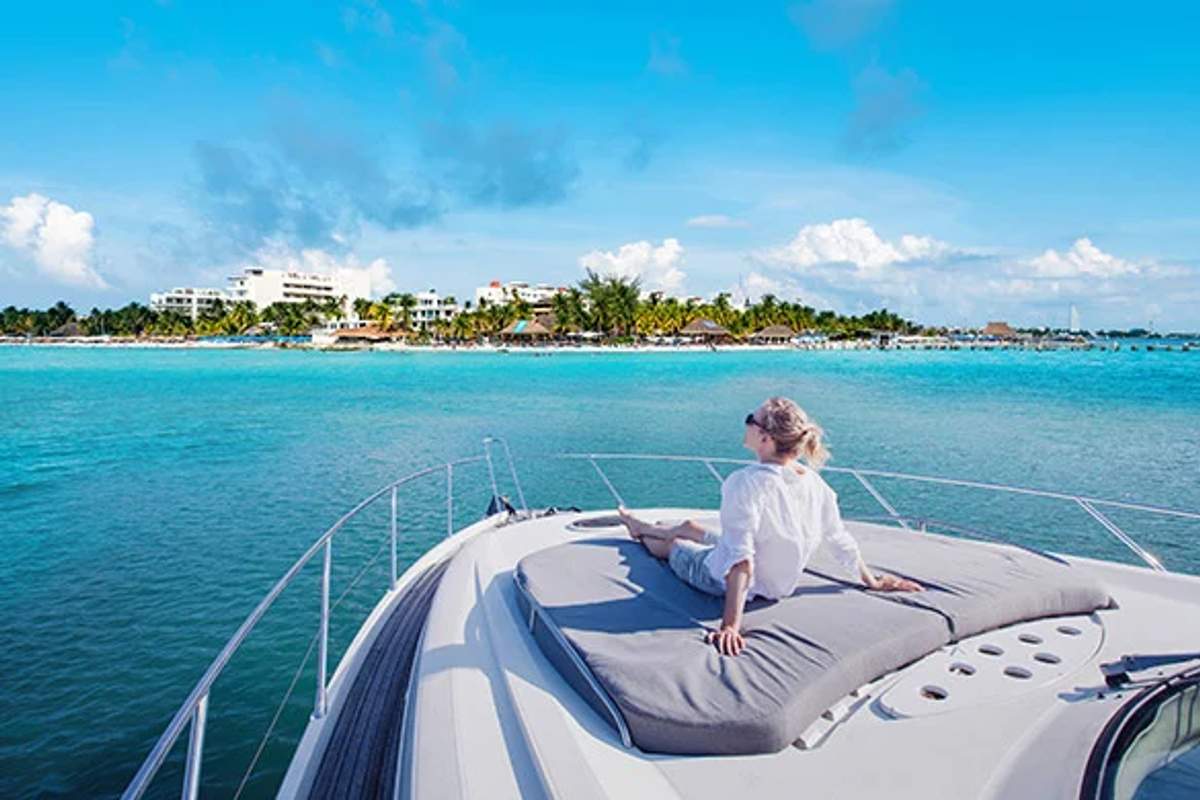 Mujer relajándose en yate con vista a la costa de Cancún en un día soleado.