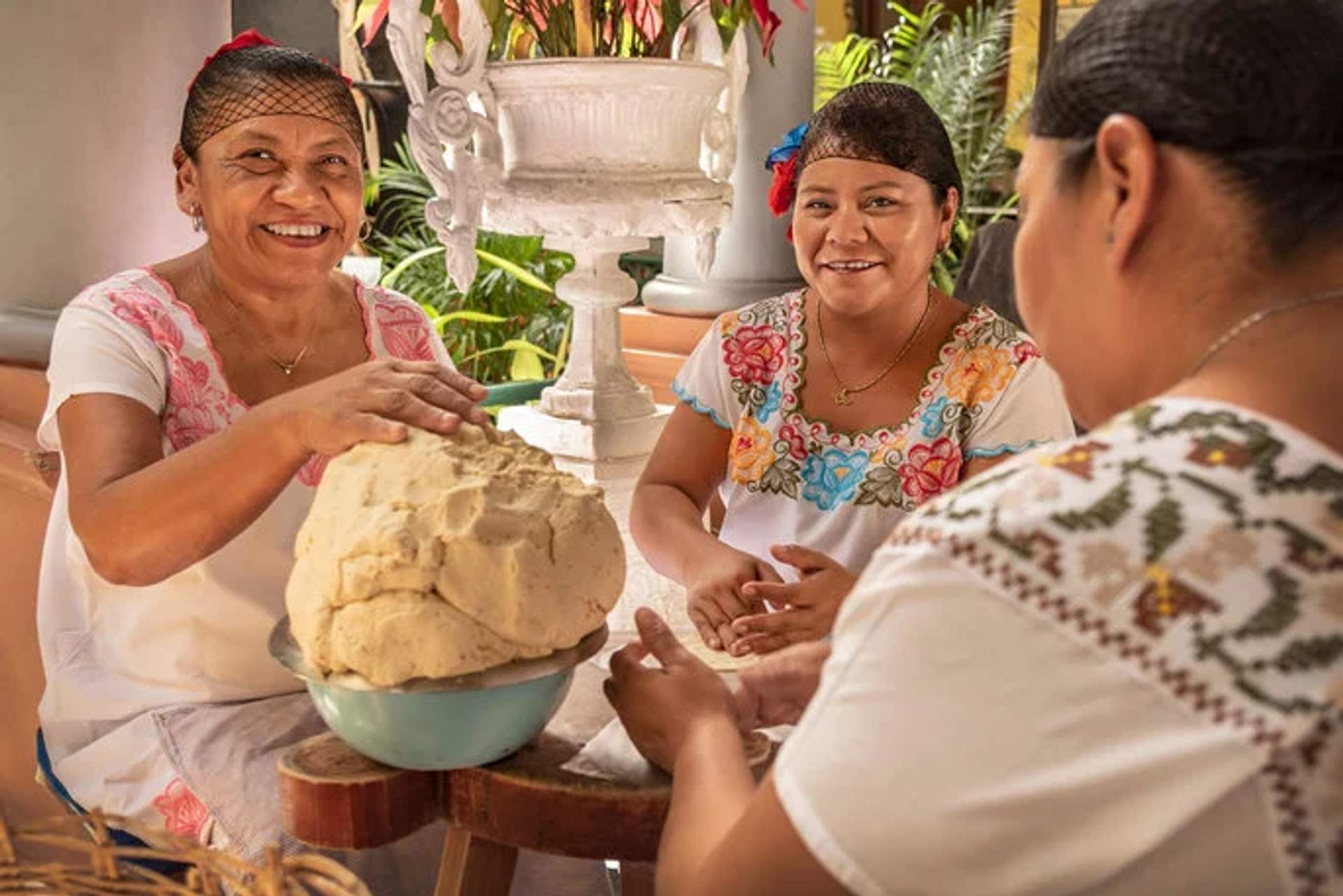 Women in traditional Mexican attire making dough by hand, smiling and enjoying the culinary experience.
