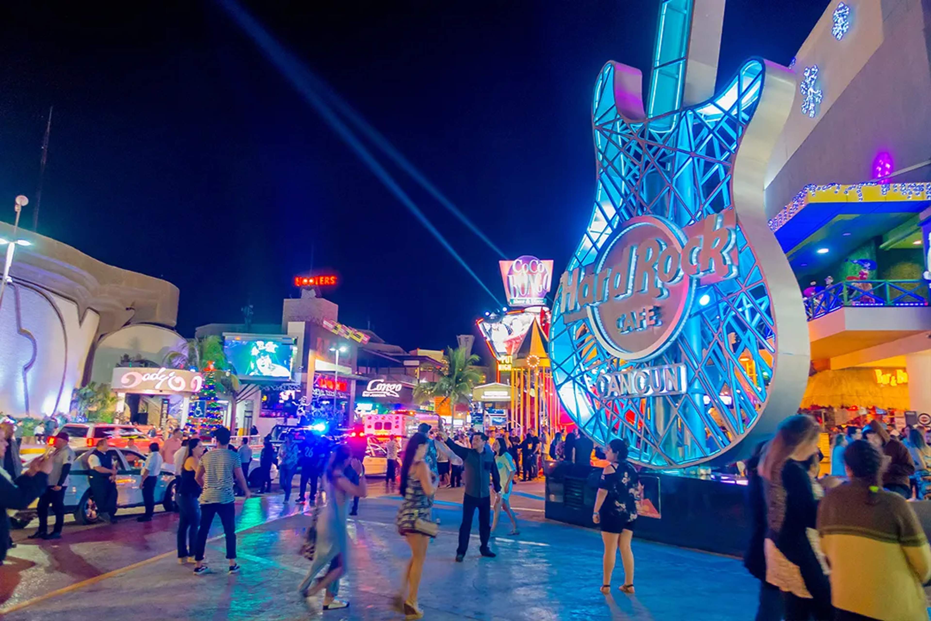 Gente disfrutando la vida nocturna de Cancún con luces brillantes y el icónico letrero de Hard Rock Café