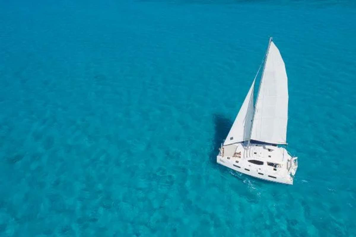 Un velero navegando sobre aguas cristalinas y turquesas. La vista aérea resalta la claridad del agua y la tranquilidad del mar abierto.
