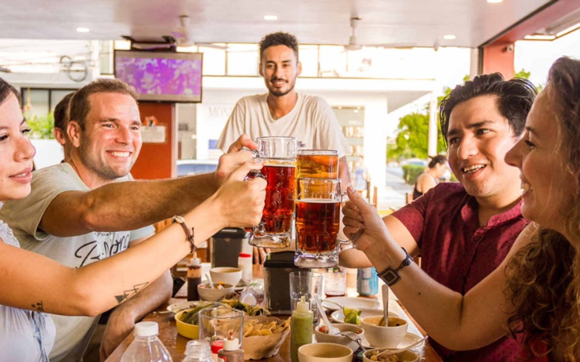 Friends enjoying a meal and toasting with beer at a local restaurant in Cancun.