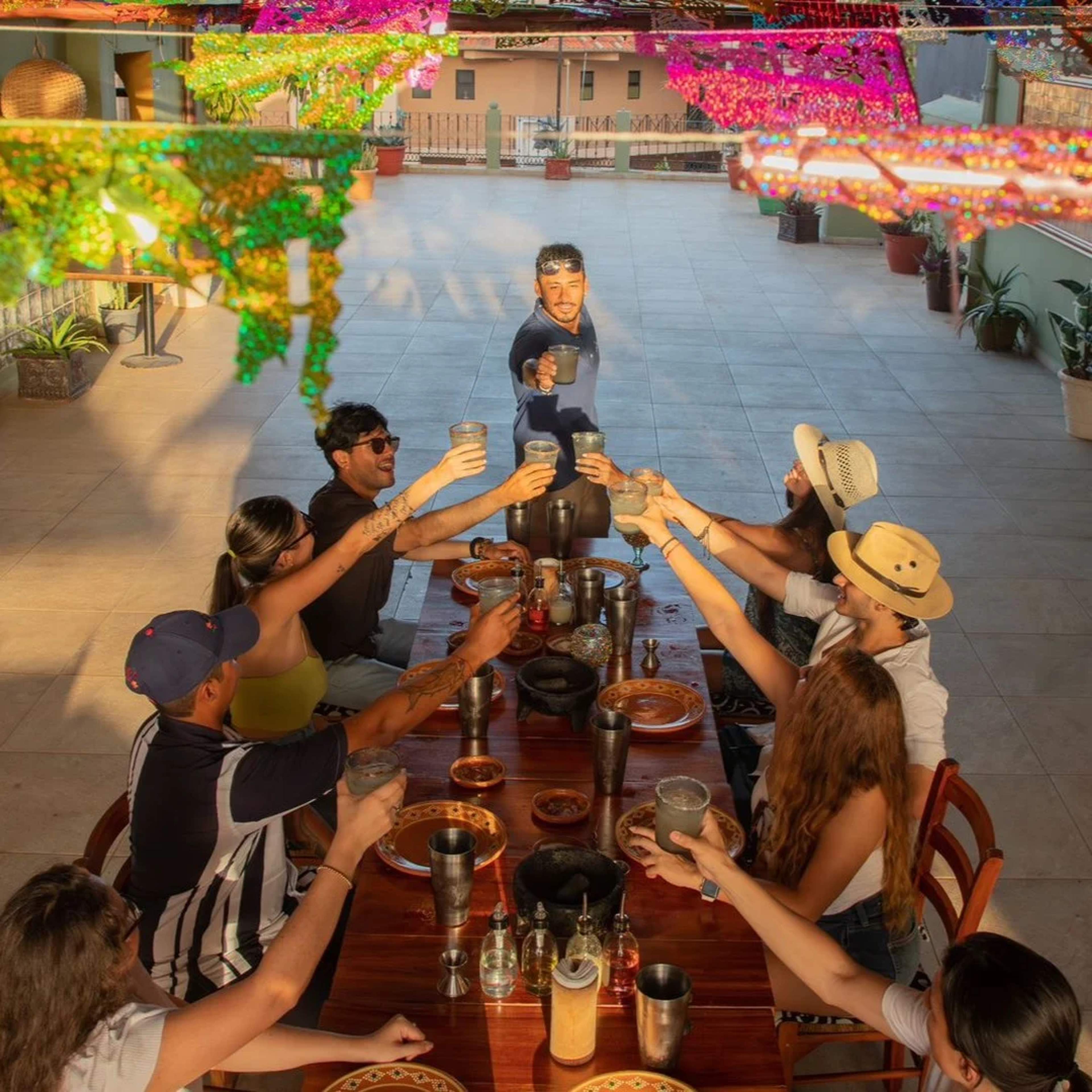 Grupo de amigos brindando en una mesa al aire libre decorada con banderines coloridos durante una comida festiva.