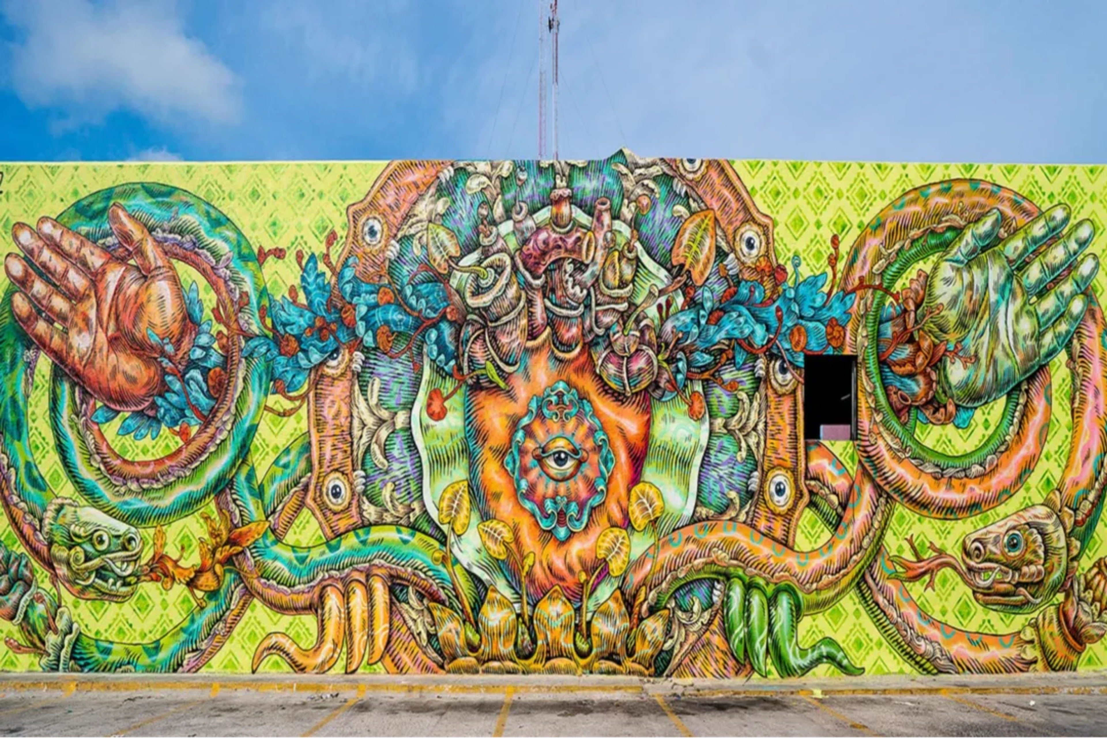 Colorido mural urbano con formas surrealistas, manos, serpientes y un ojo central simbólico.
