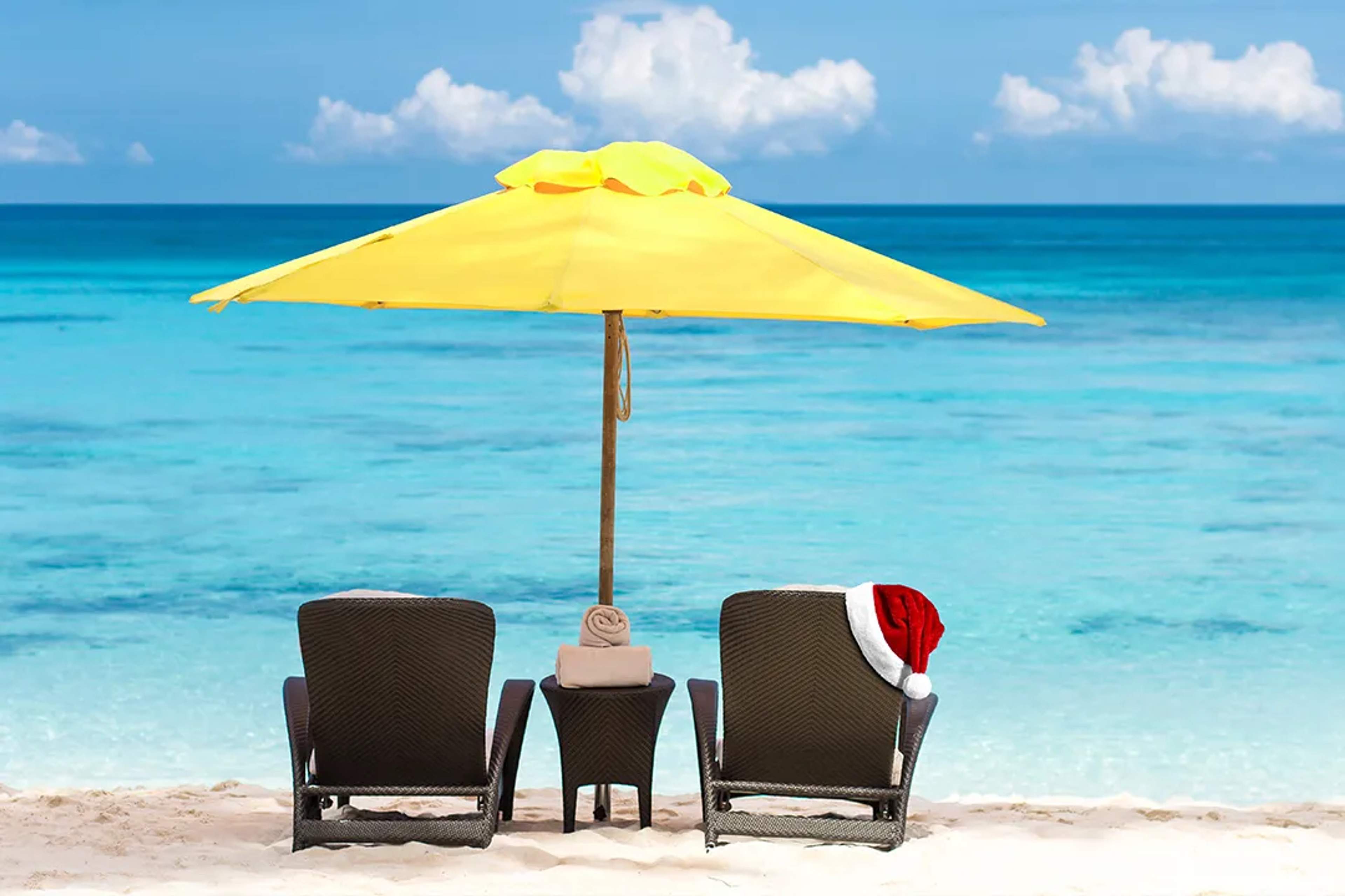 Beach chairs under a yellow umbrella facing turquoise water, with a Santa hat for a tropical holiday vibe