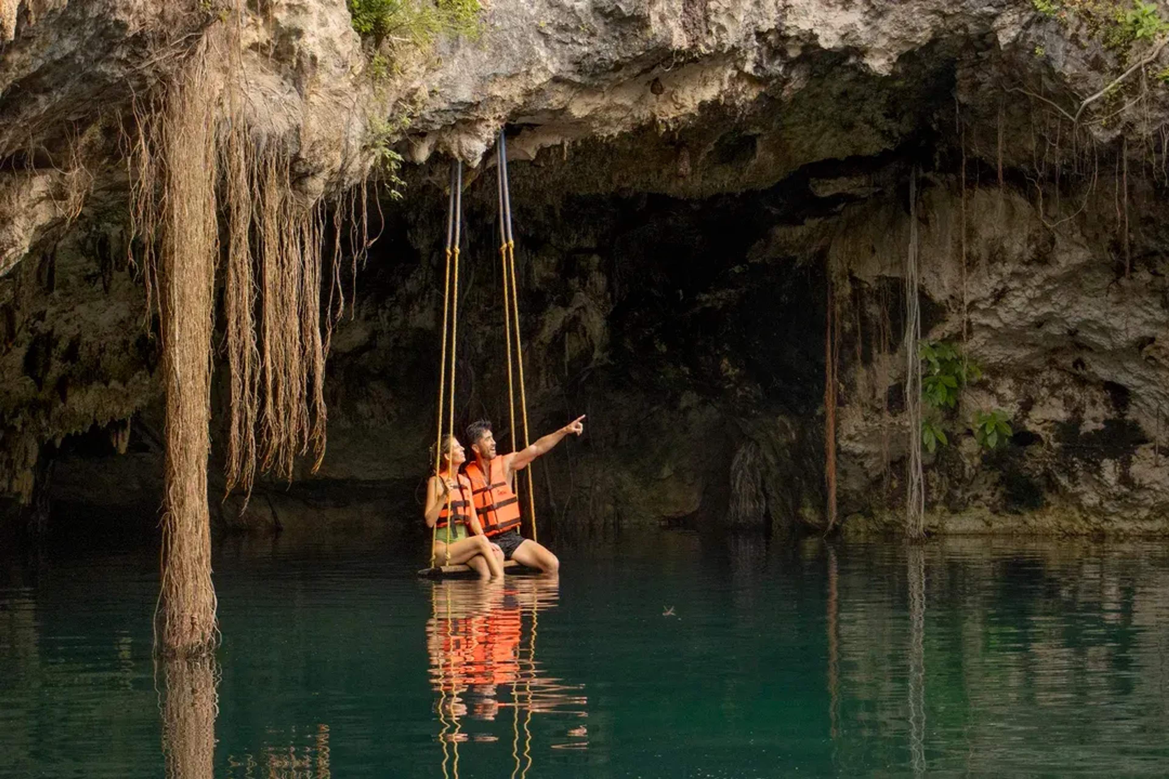 Couple on a swing above a cenote, surrounded by jungle vines and crystal-clear water.