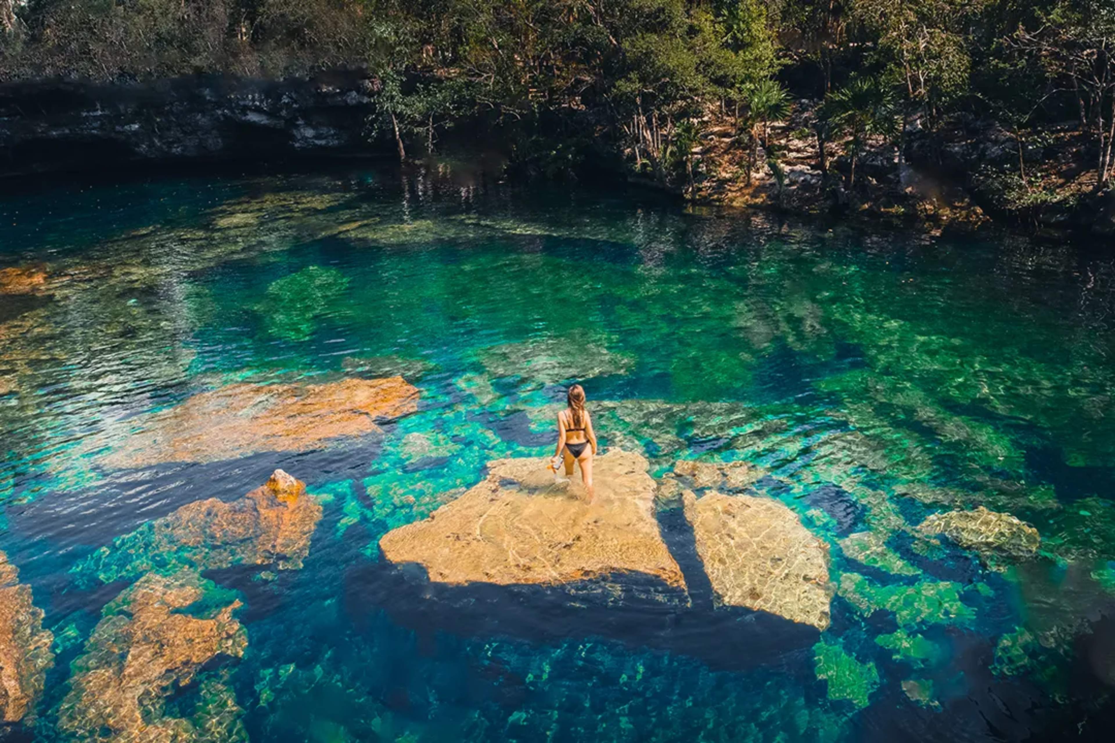 Mujer explorando un cenote maya de aguas cristalinas rodeado de selva, un paisaje natural sagrado y sereno