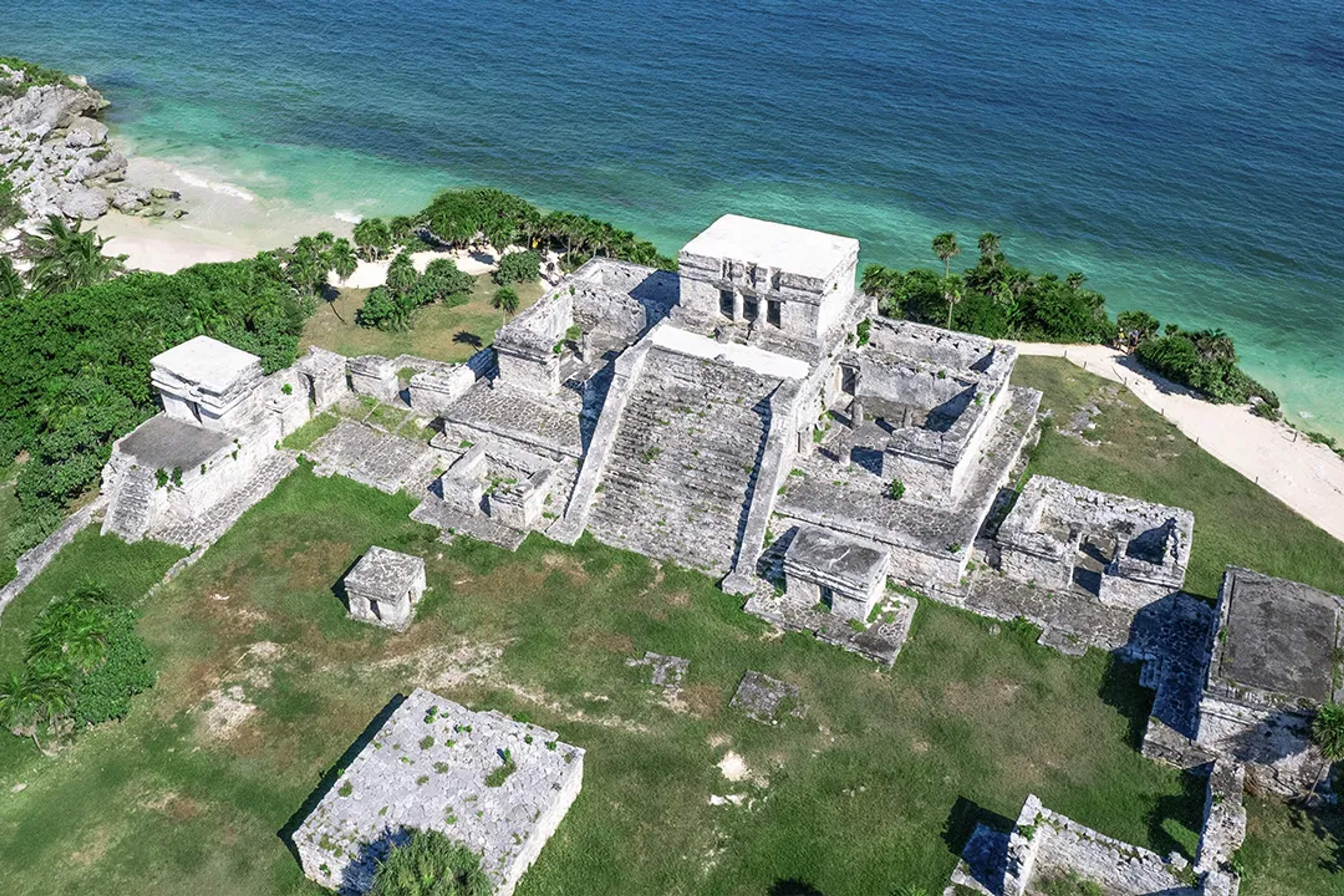 Aerial view of the Tulum ruins by the sea, showcasing ancient Mayan structures and turquoise water.