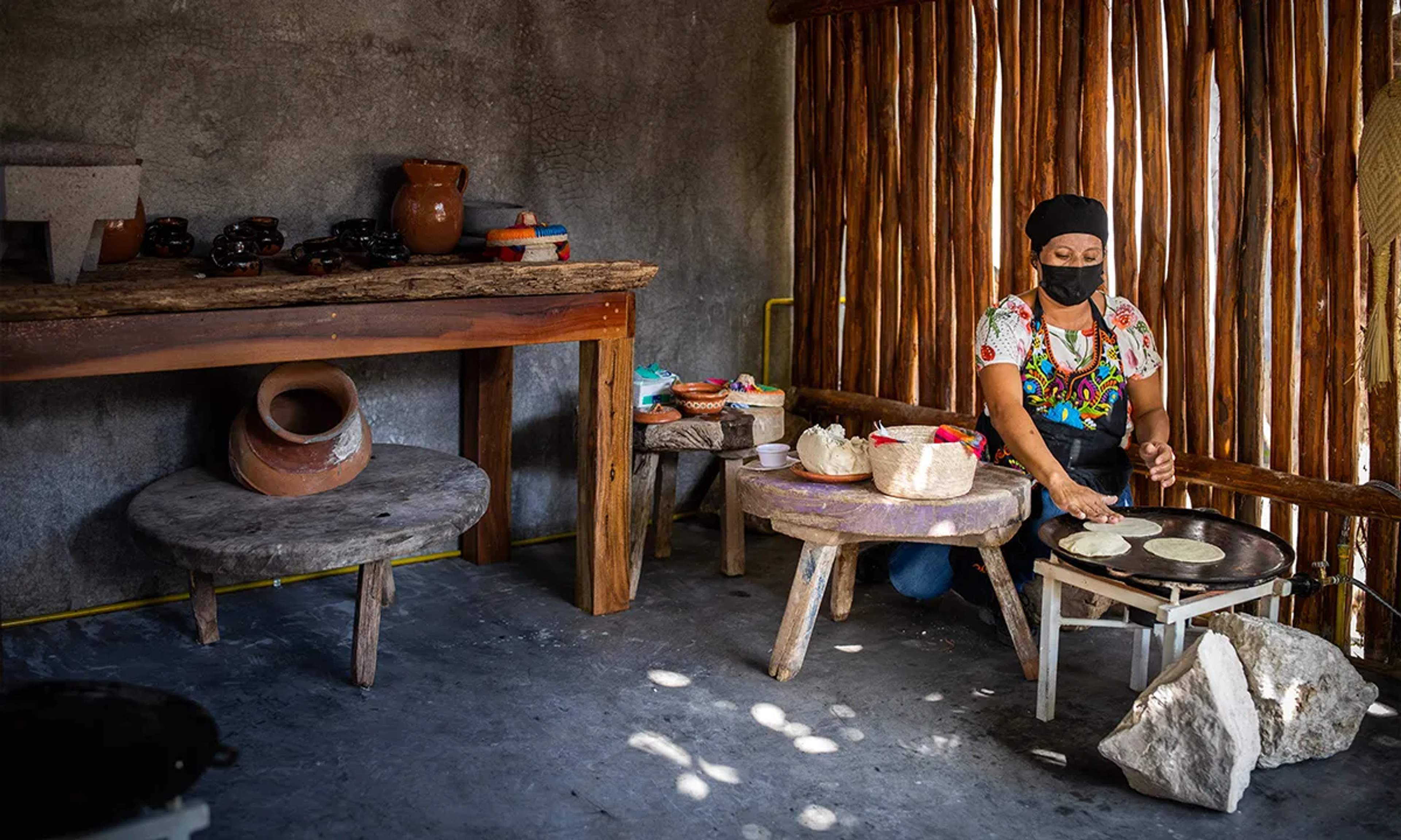 Una mujer local prepara tortillas hechas a mano en una cocina tradicional, destacando los sabores y la cultura de la Riviera Maya.