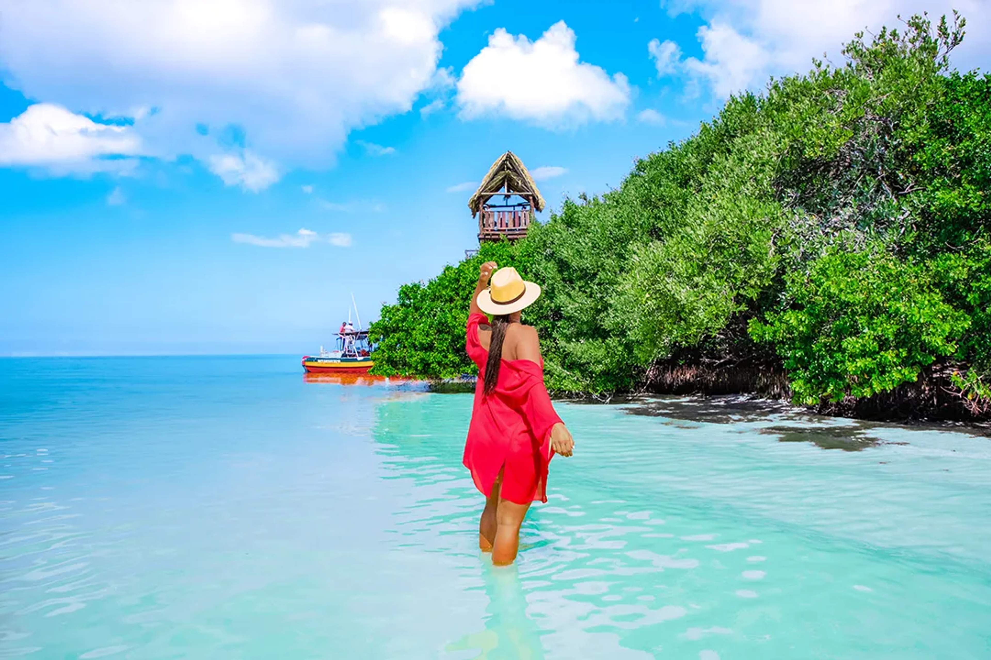 Woman walking in shallow turquoise water toward mangroves and lookout tower during a Holbox adventure