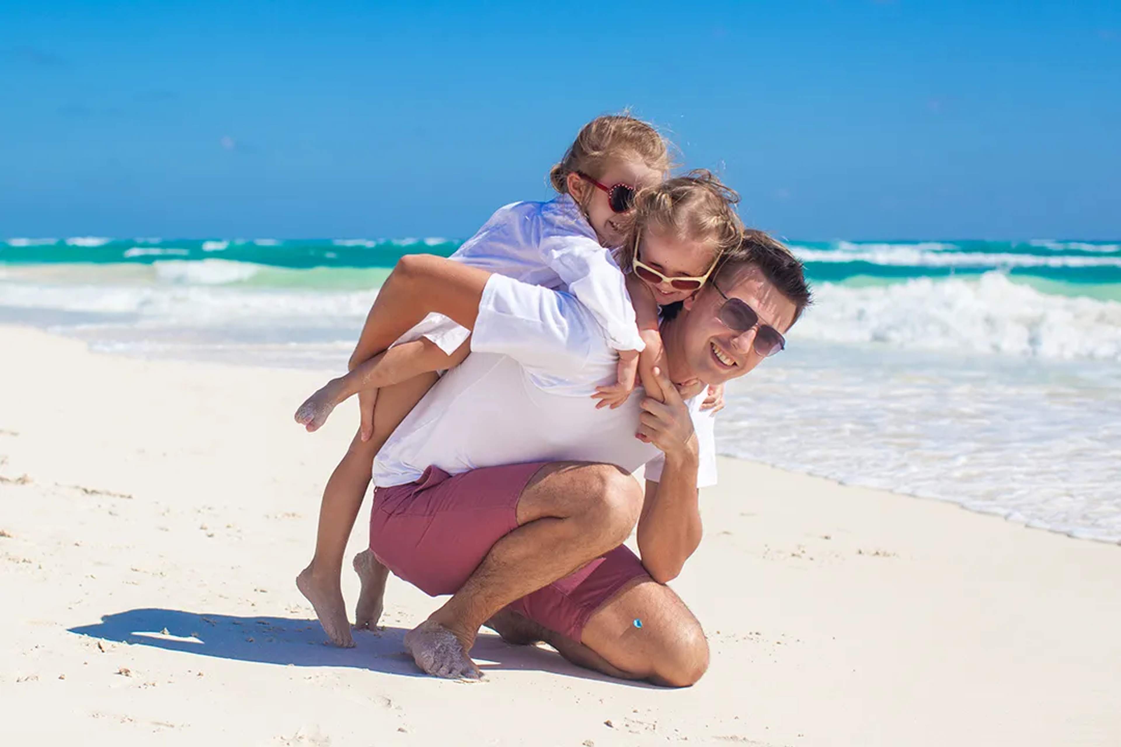 Father playing with his children on a white sand beach in Cancun, enjoying waves, sunshine, and a joyful family moment