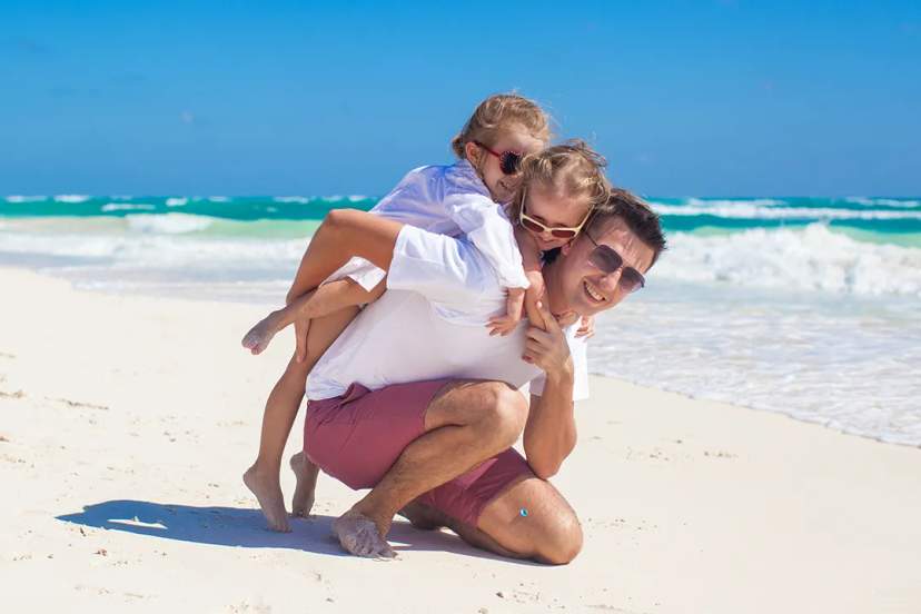 Father playing with his children on a white sand beach in Cancun, enjoying waves, sunshine, and a joyful family moment