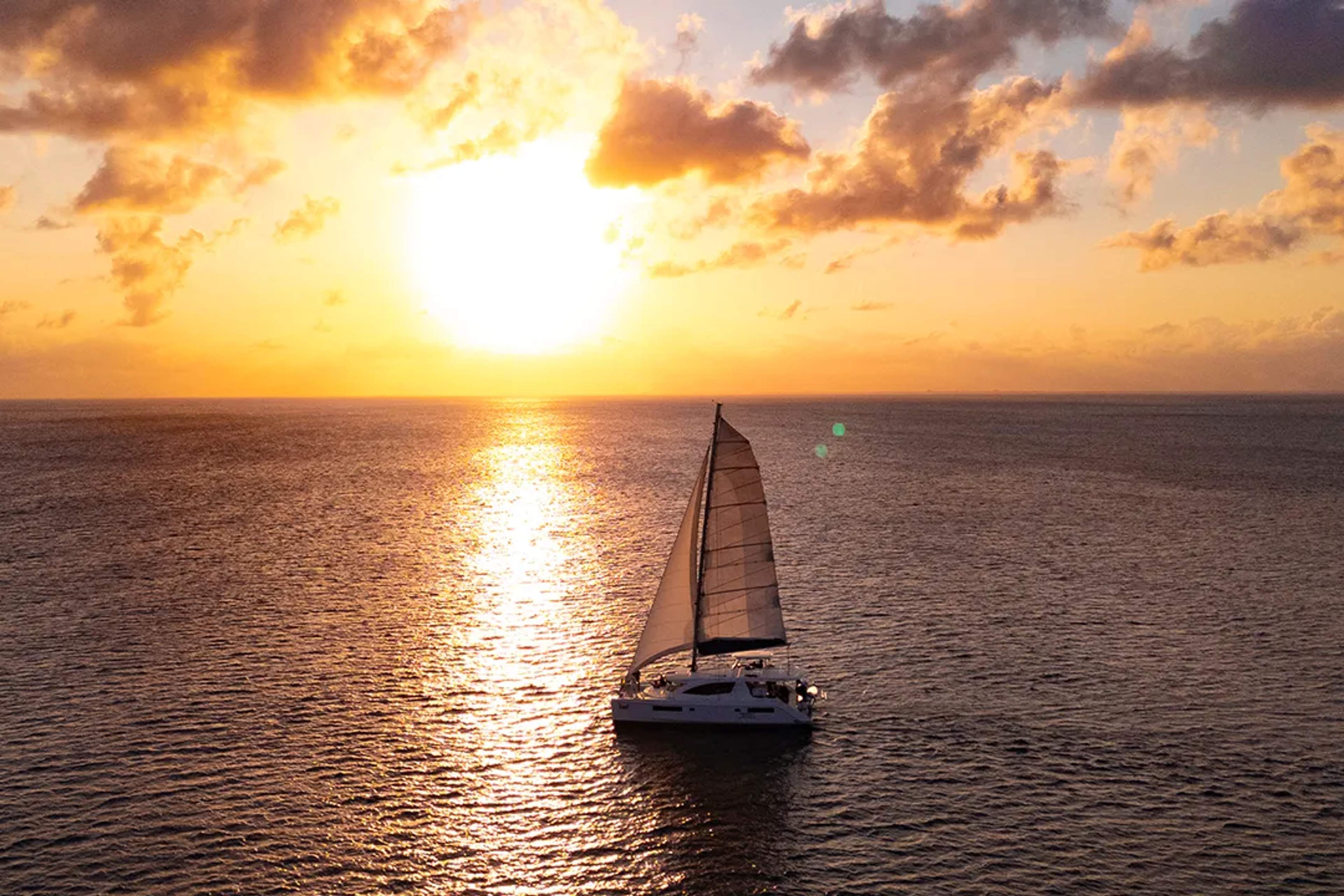 Sunset catamaran sailing tour on the ocean, golden sky and calm sea, romantic cruise experience glow